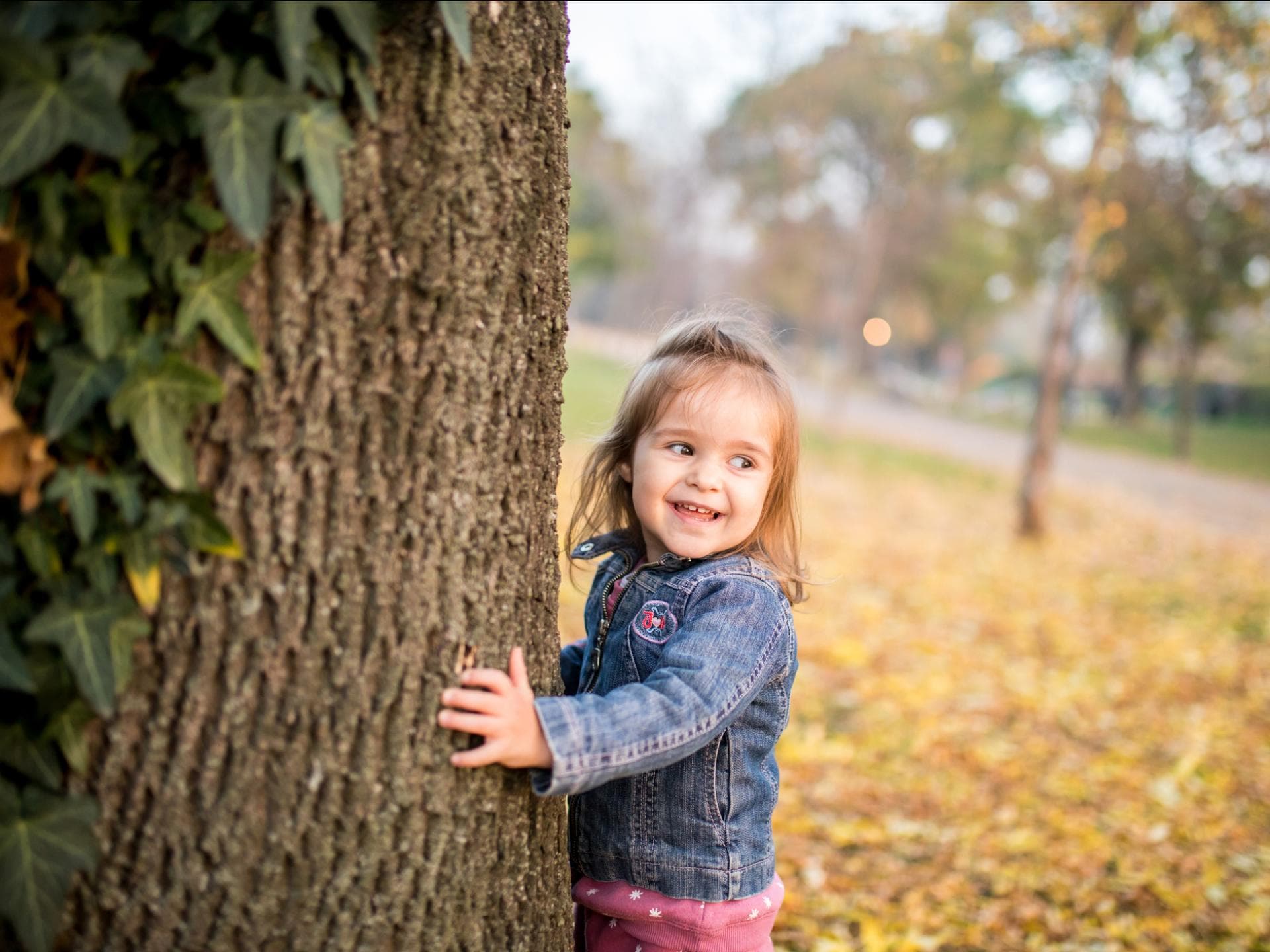 Fröhliches Kind läuft um Efeu-berankten Baum