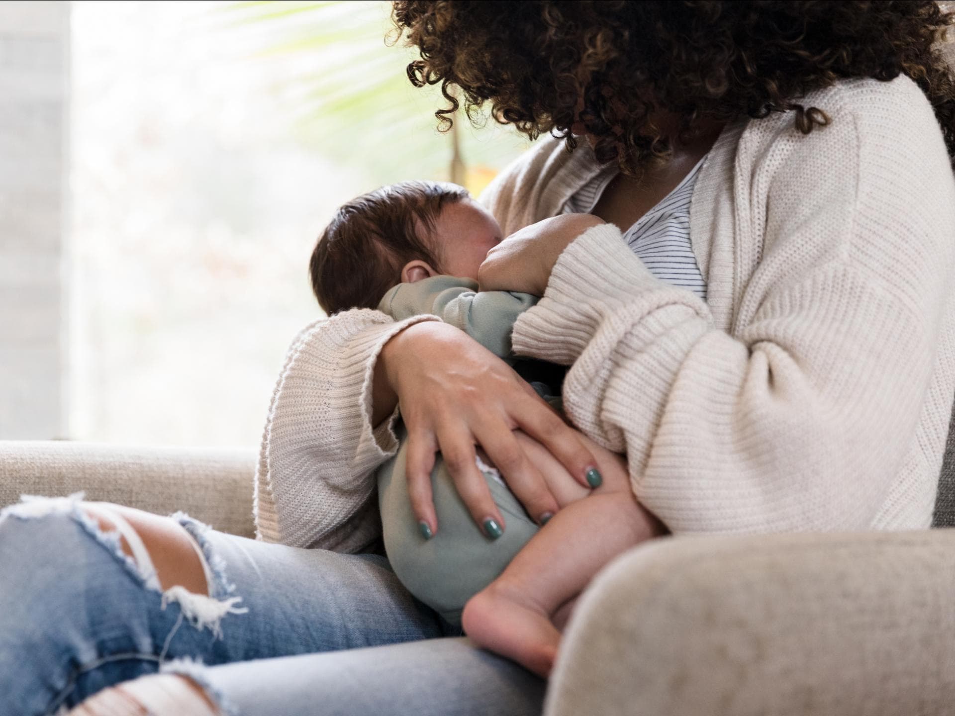 Eine Frau stillt ihr Baby sitzend auf dem Sessel.
