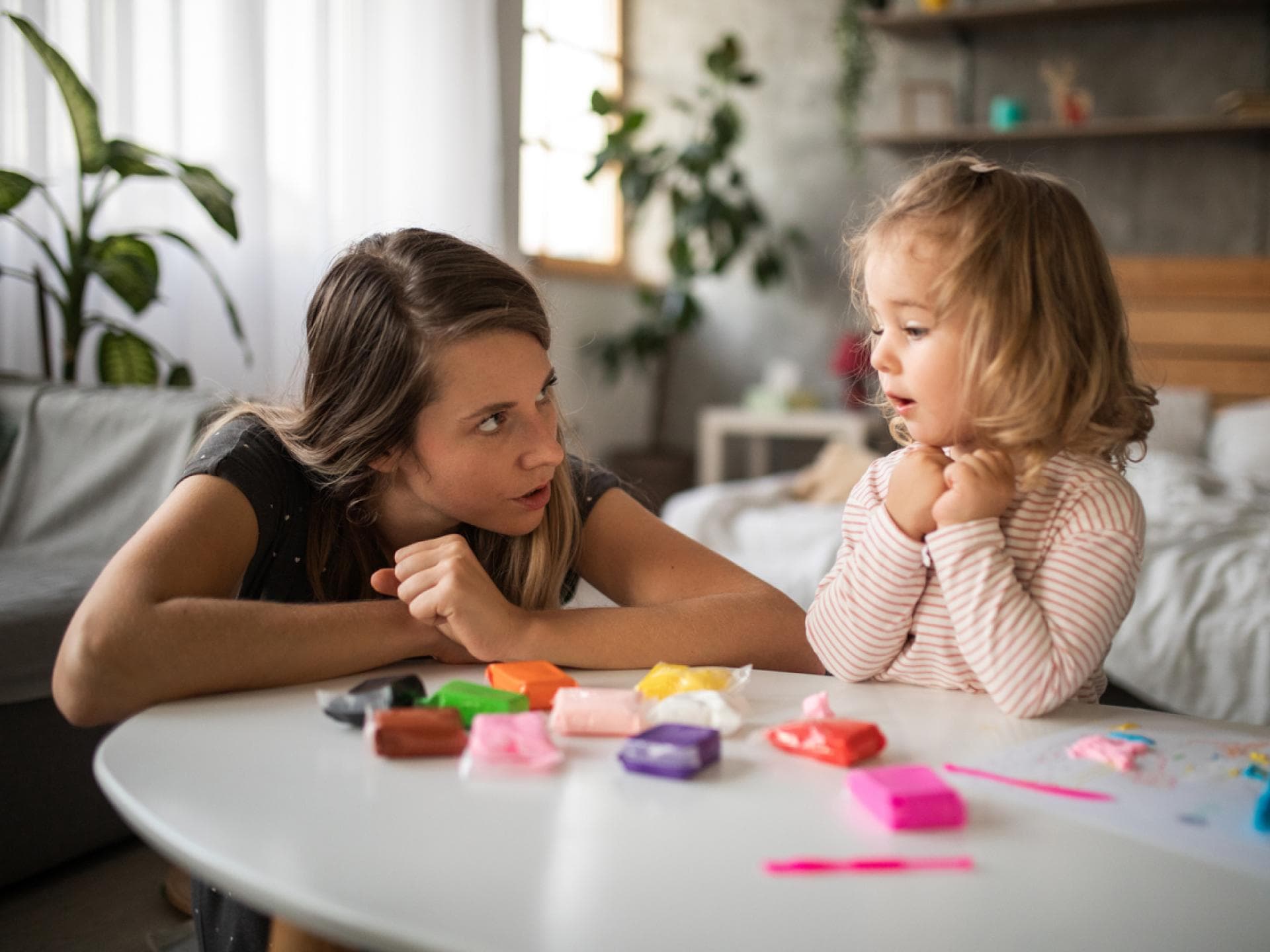 Mutter spricht mit ihrer kleinen Tochter am Spieltisch.