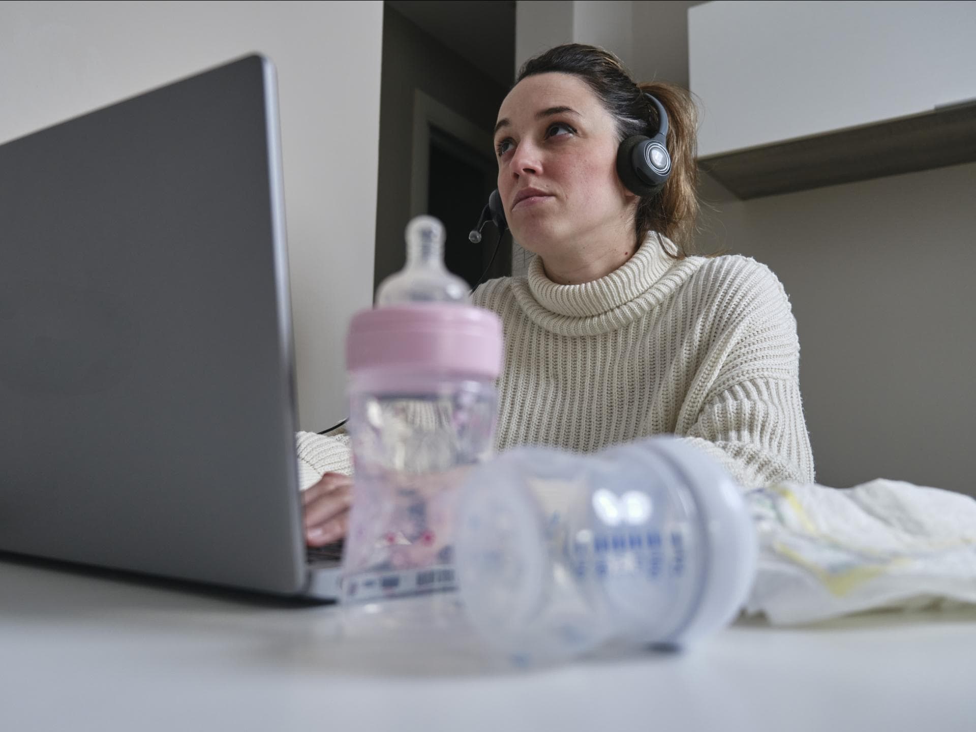 Mutter sitzt mit Milchflaschen und Windeln am Laptop.
