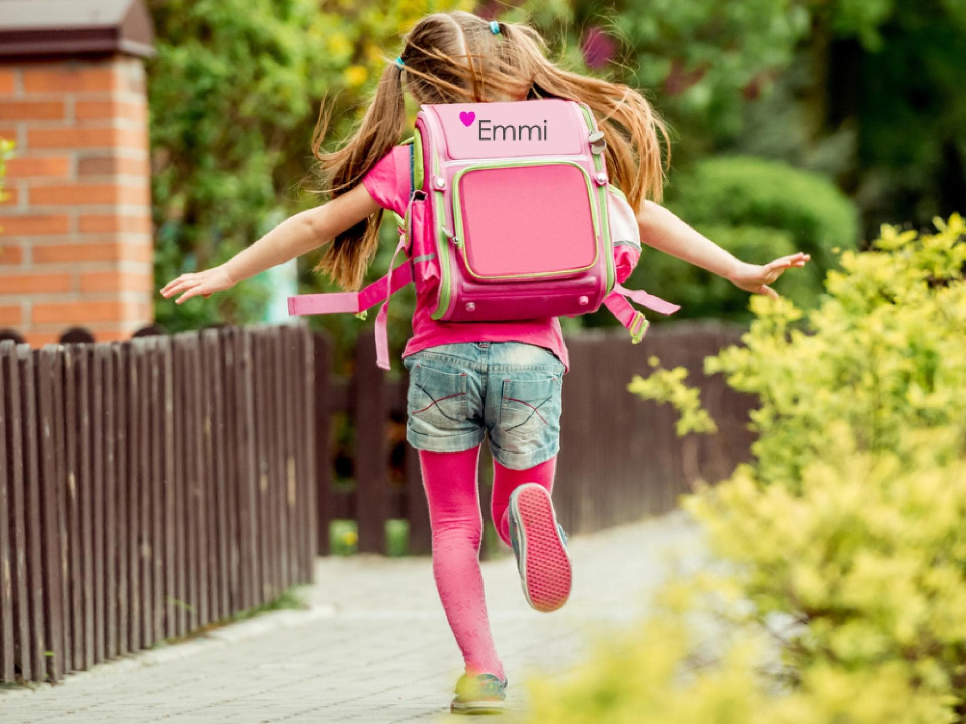Mädchen mit einem bestickten Schulranzen läuft den Gehweg entlang.