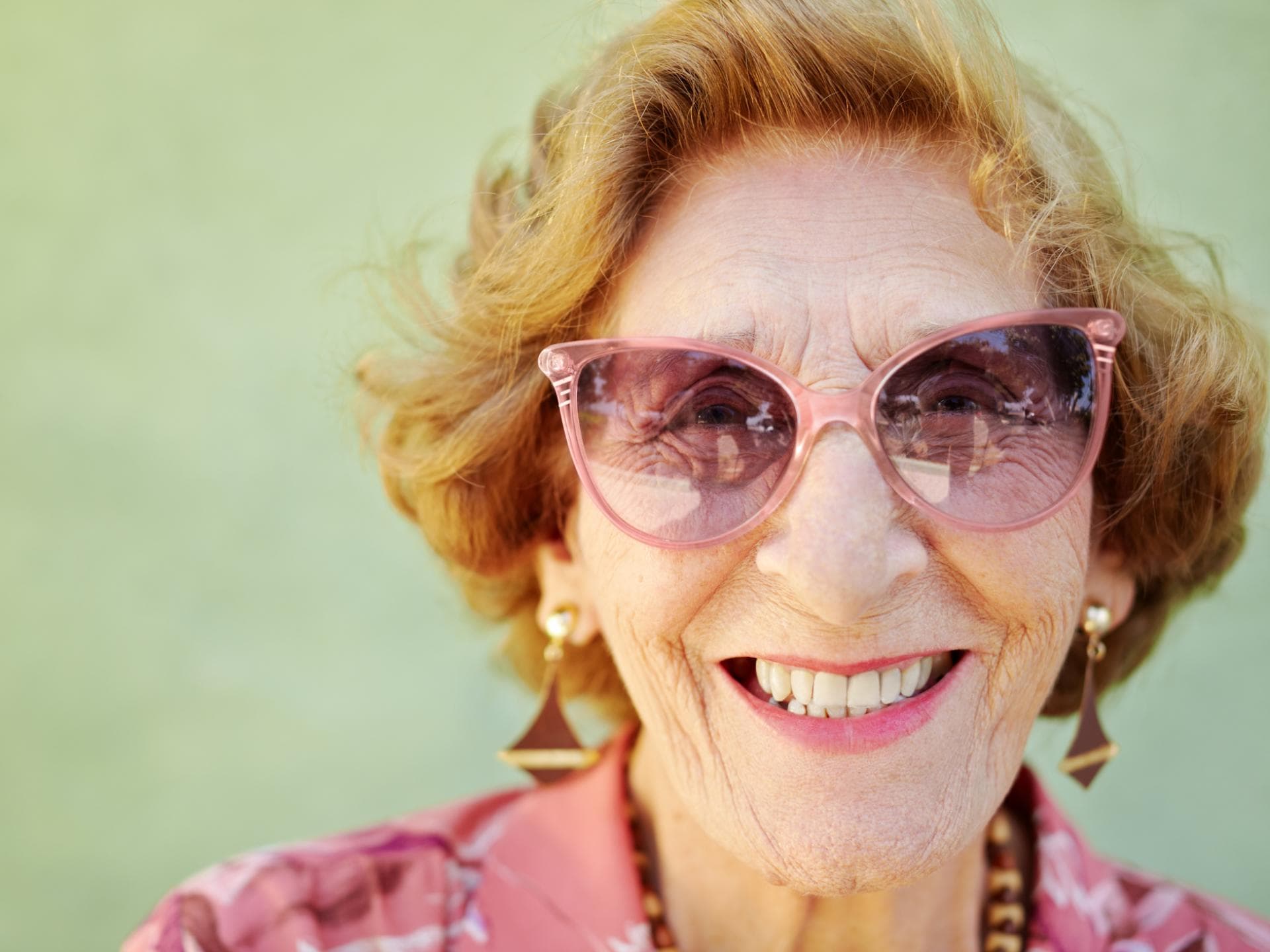Lachende alte Frau mit rosa Sonnenbrille.
