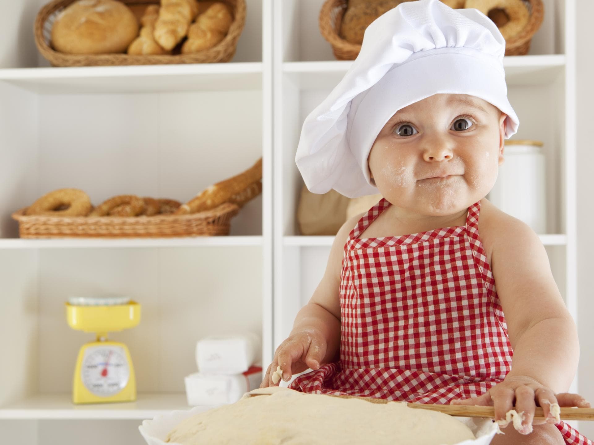 Baby mit Bäckermütze macht Brotteig.