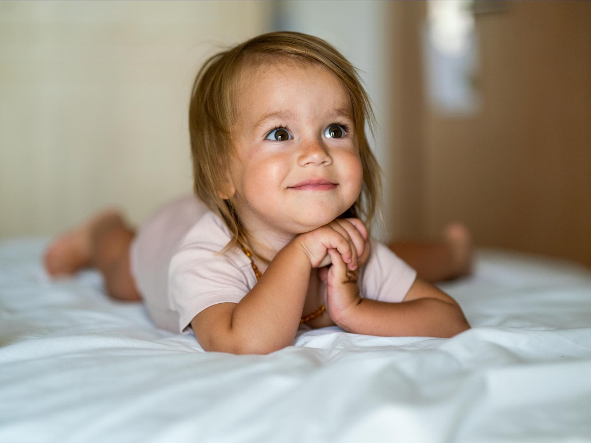 Ein kleines Mädchen liegt grinsend auf dem Bett und schaut aufgeregt. Ein kleines Mädchen liegt grinsend auf dem Bett und schaut aufgeregt.