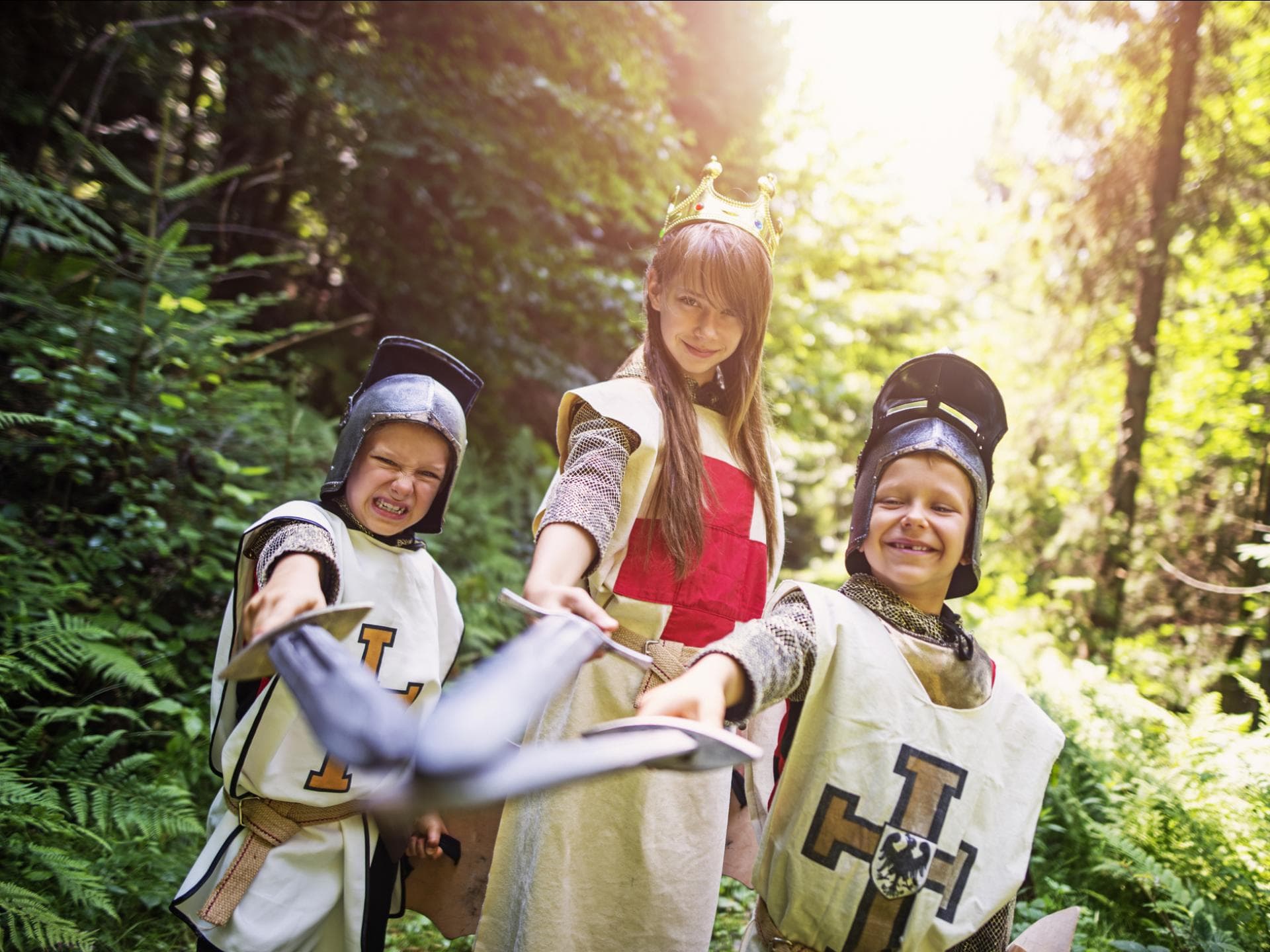 Zwei Jungs und ein Mädchen sind verkleidet als Ritter und Königin im Wald.