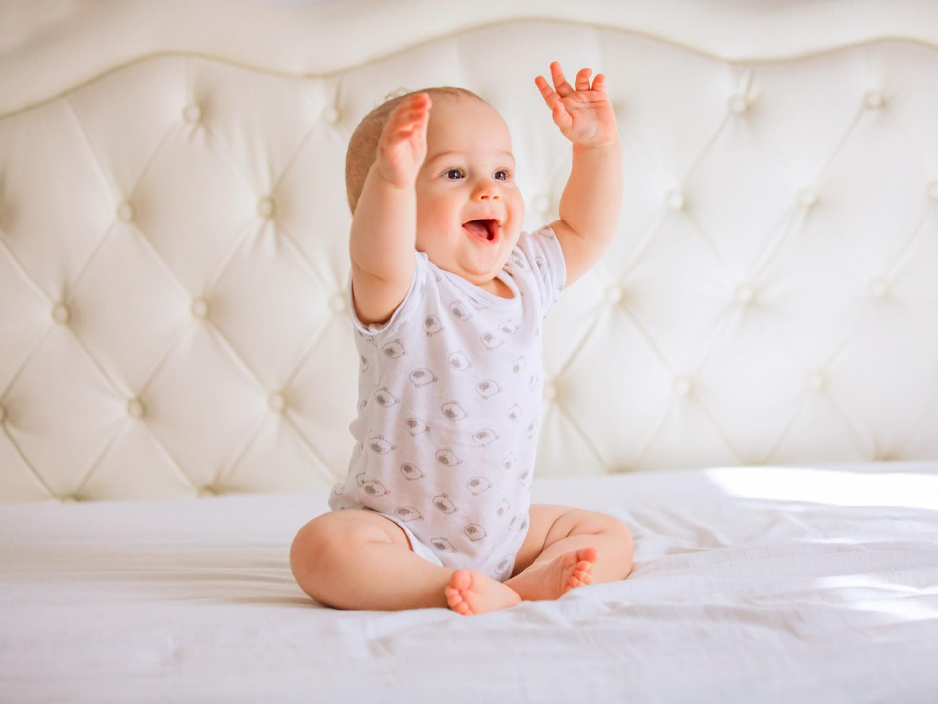 Baby sitzt lachend auf dem Bett.