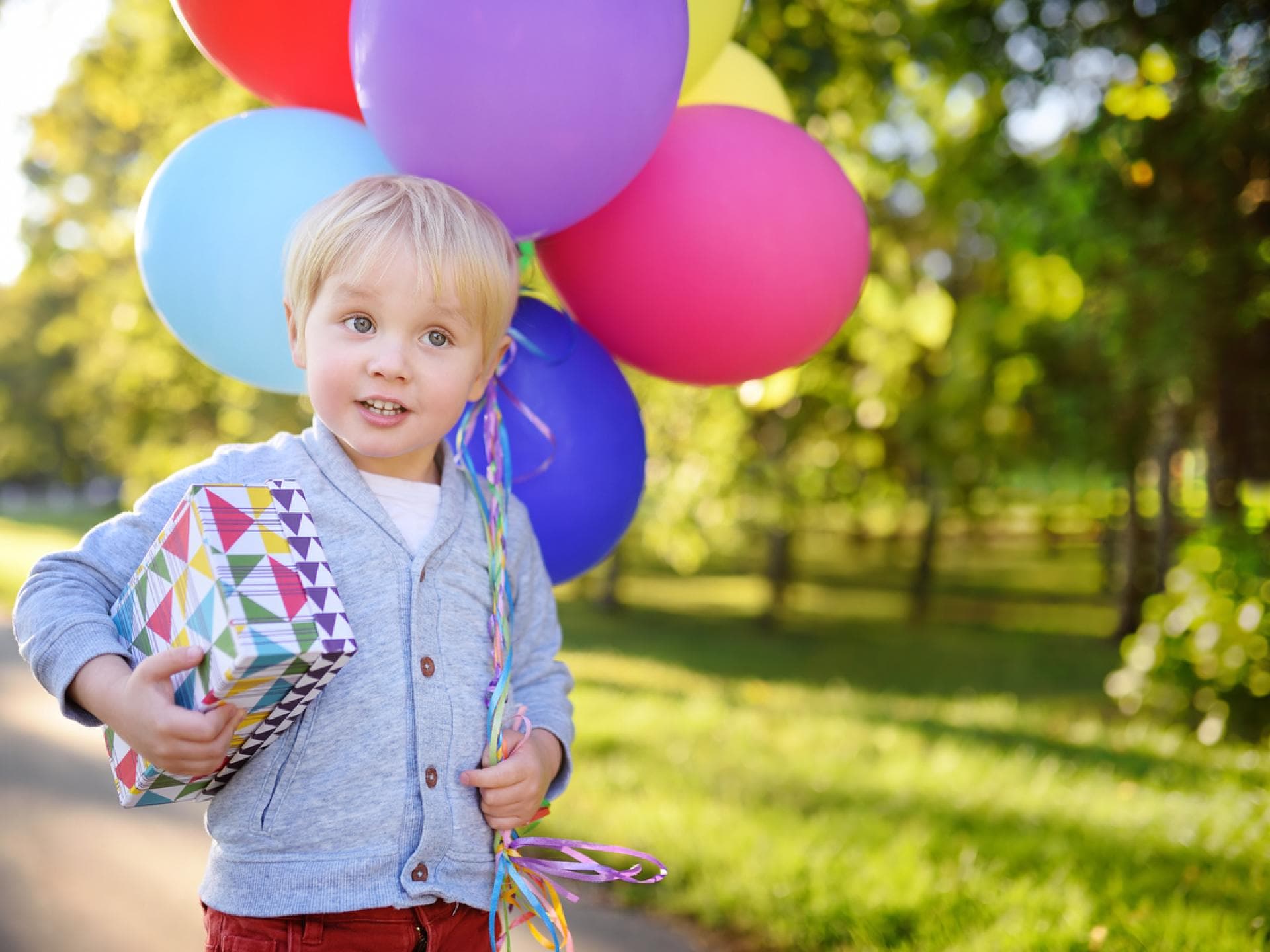 Kleiner blonder Junge feiert 3 Geburtstag und trägt Ballon und Geschenk. 