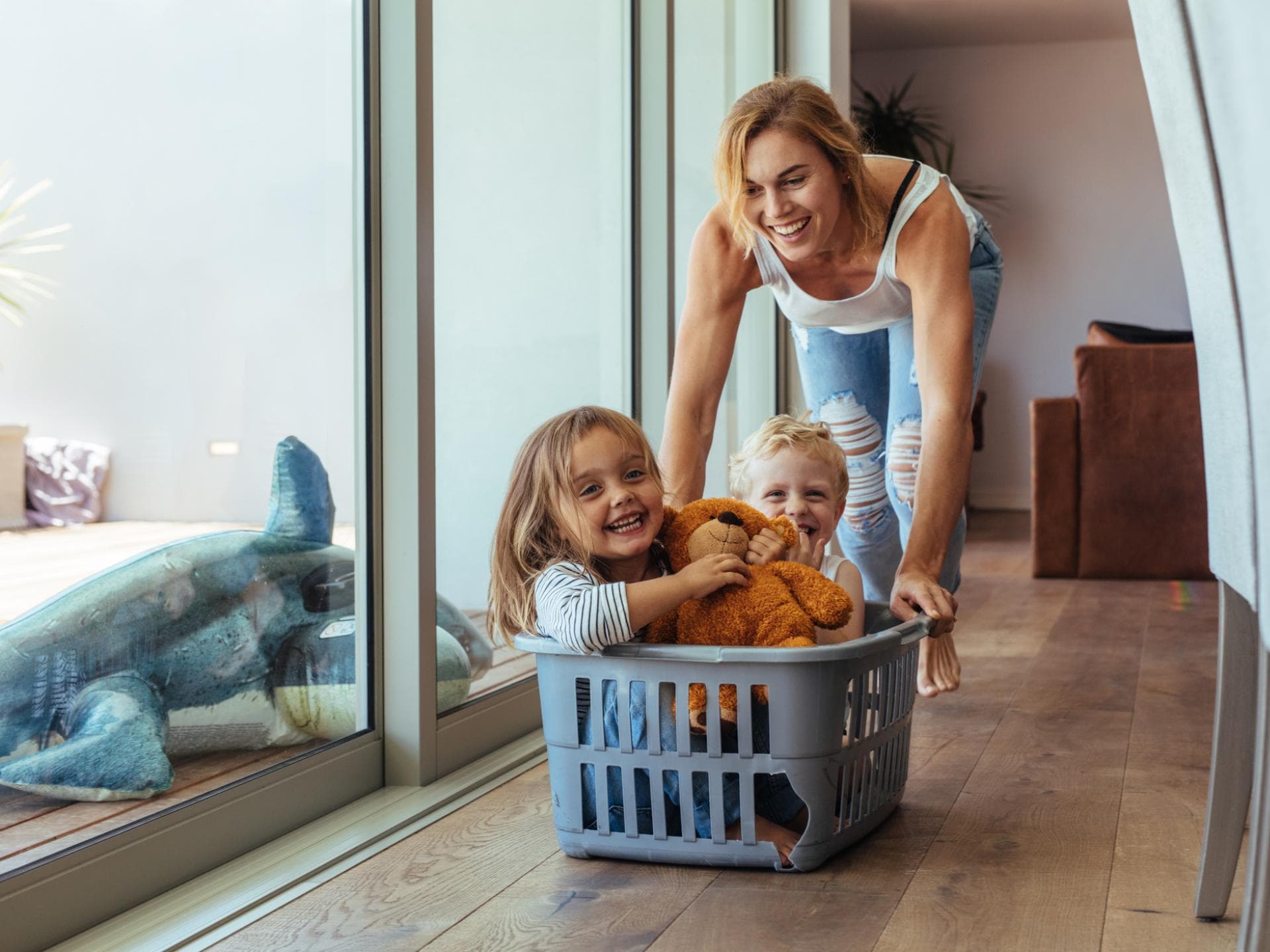 Lachende Mutter schiebt ihre Kinder in einem Wäschekorb.