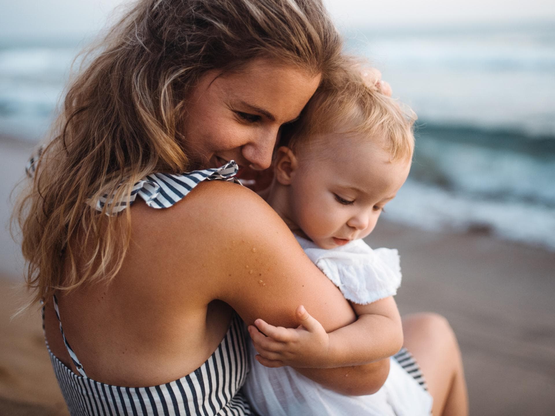 Mama kuschelt mit Baby bei Reise am Strand