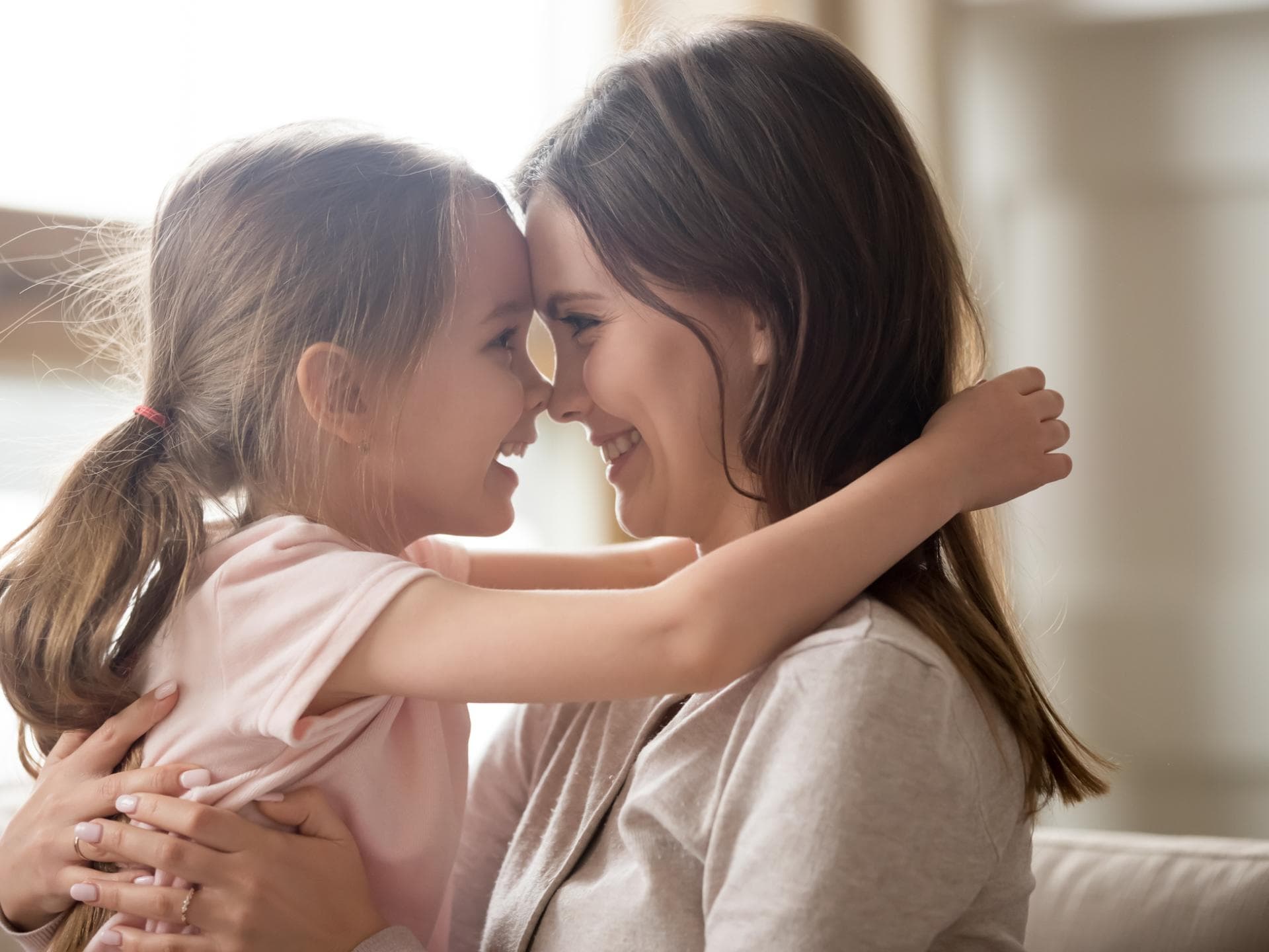 Emotionale Intelligenz lernen Kinder durch Vorbild. Kind umarmt lächelnde Mutter, ihre Nasen berühren sich.