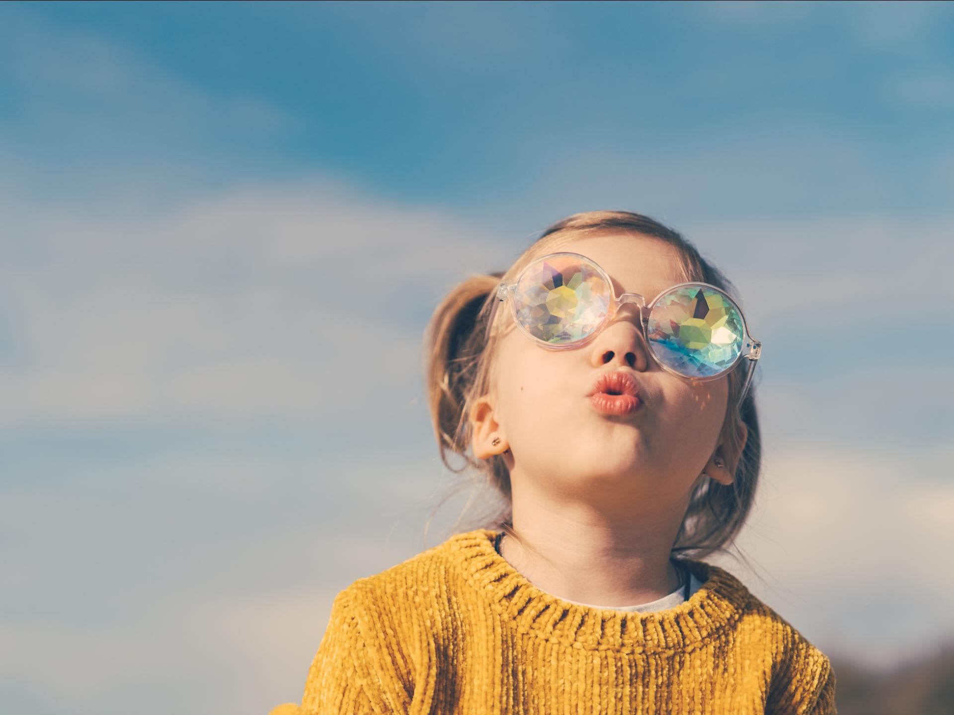 Ein kleines Mädchen schaut mit dicker Sonnenbrille in den Himmel.