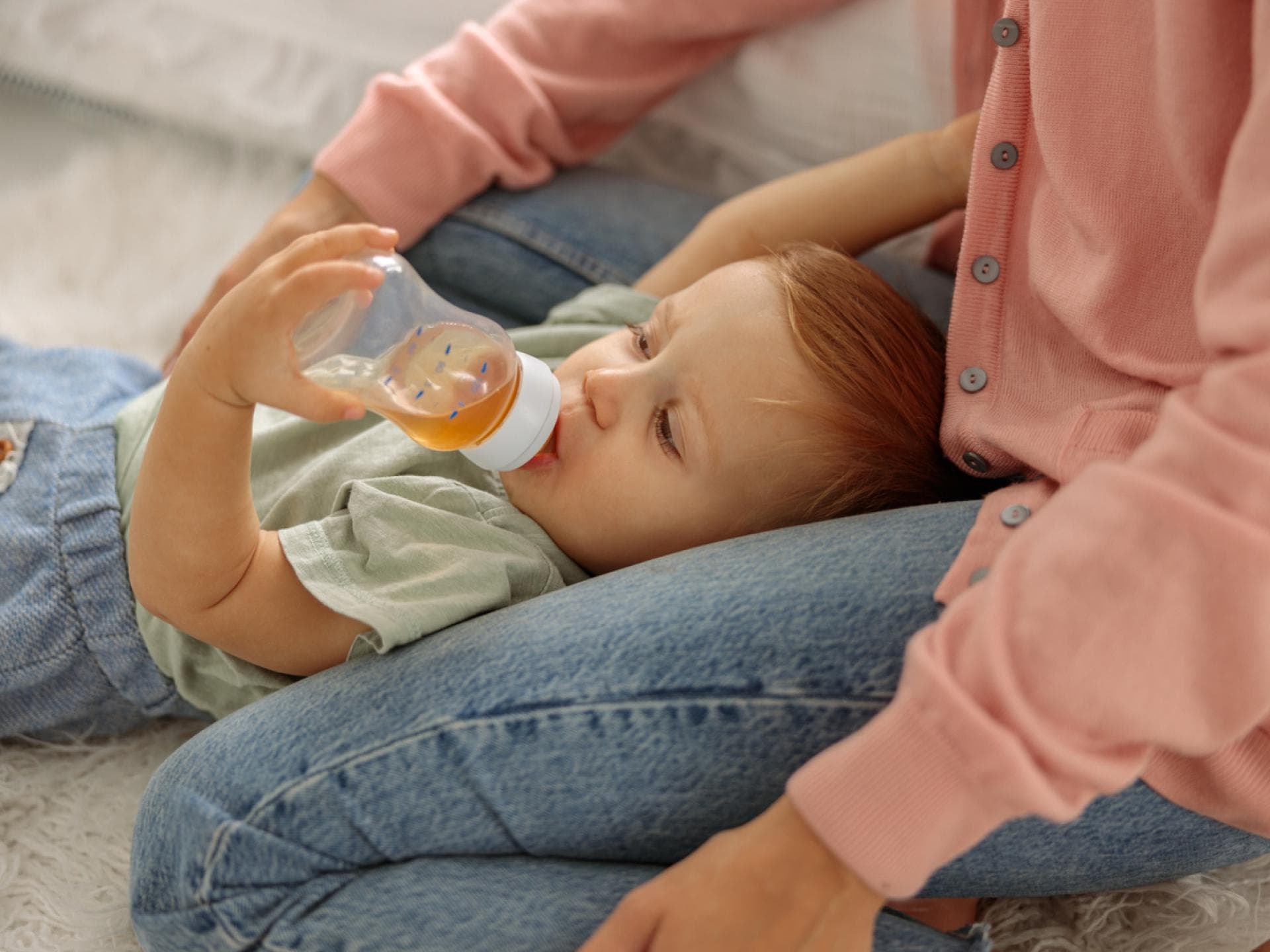Ein kleiner Baby-Junge trinkt liegend Fencheltee aus einer Nuckelflasche. 