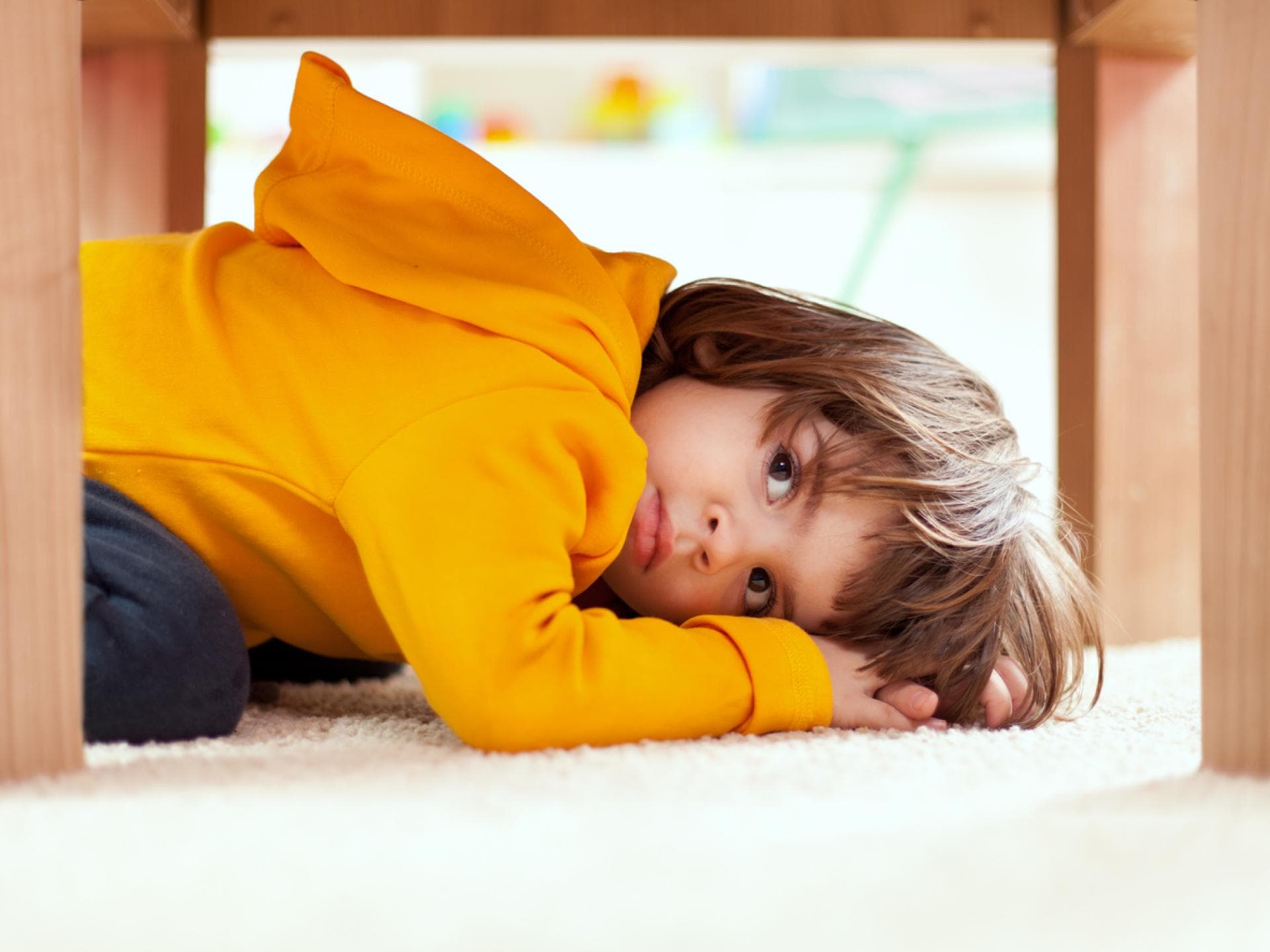 Kleiner Kita-Junge versteckt sich unter einem Tisch. Kleiner Kita-Junge versteckt sich unter einem Tisch.