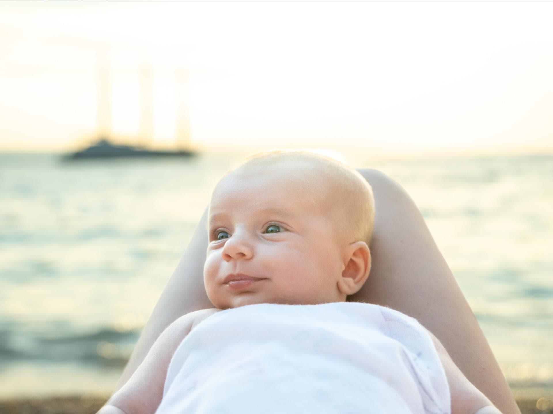 Am Meer: Ein Baby liegt zufrieden auf dem Schoss