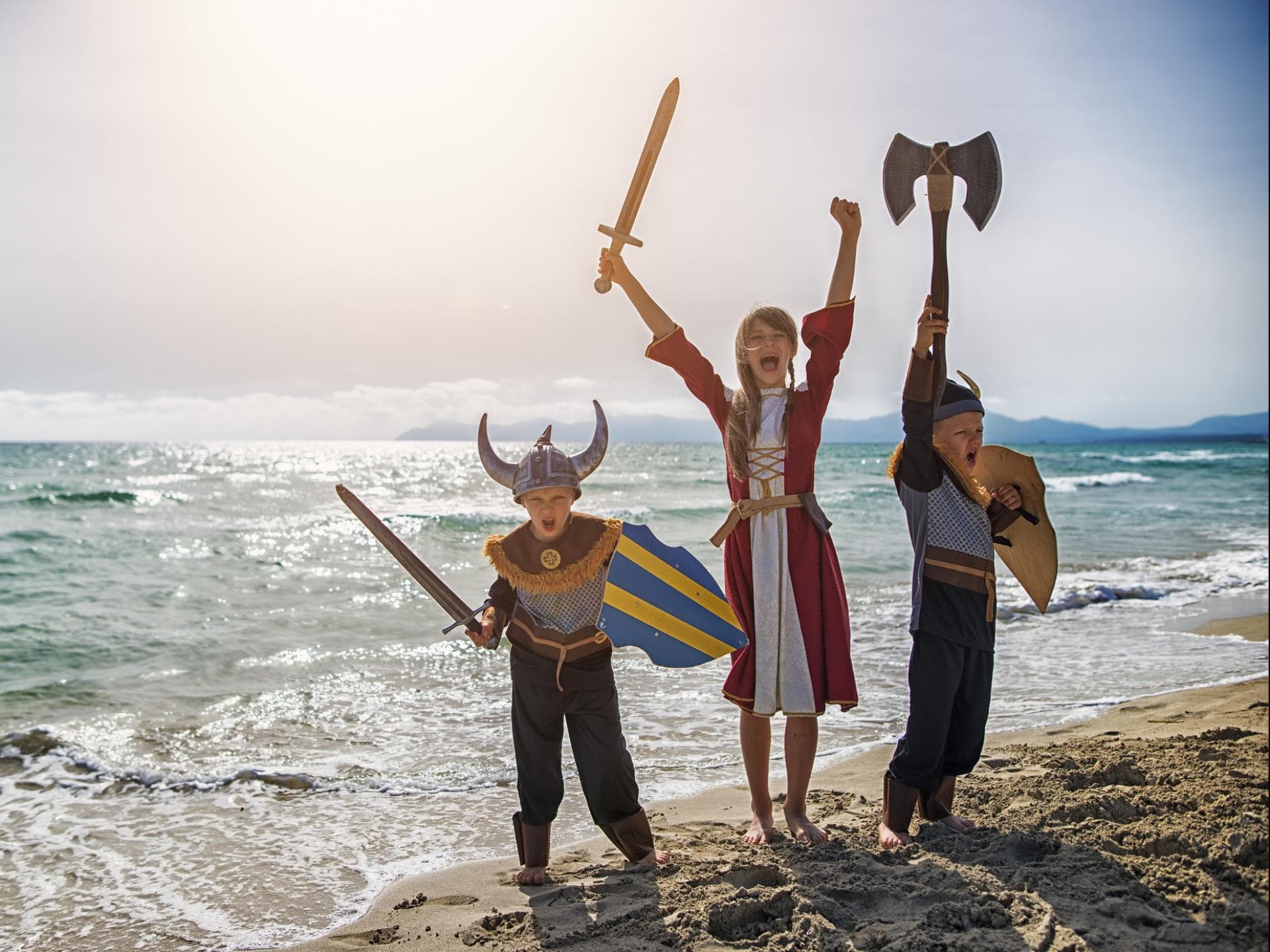 Zwei Jungen und ein Mädchen sind verkleidet als Wikinger am Strand.