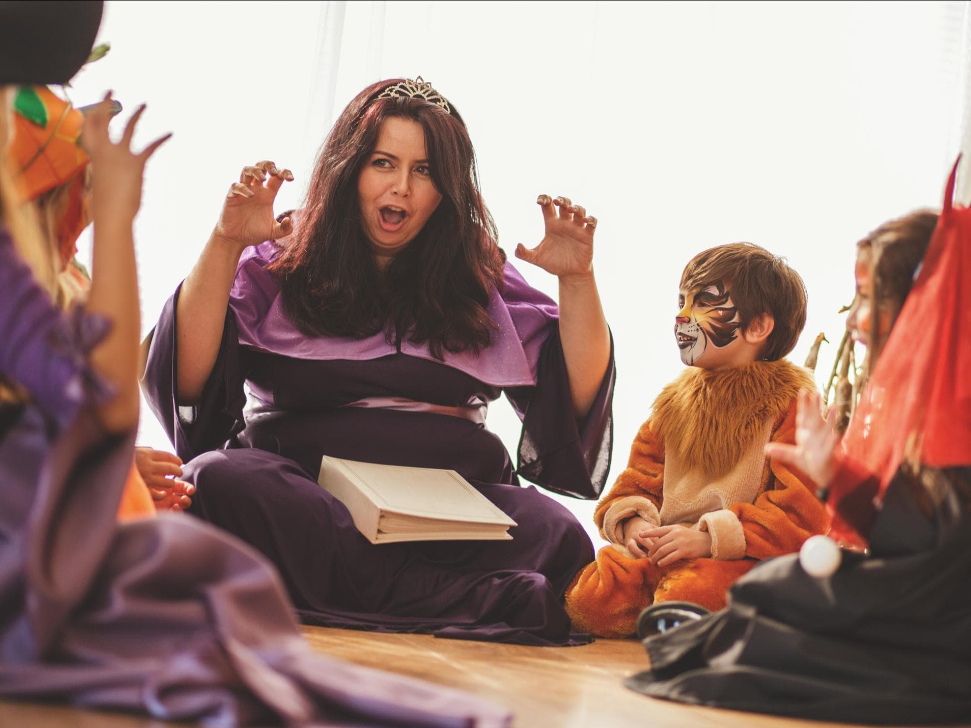 Eine verkleidete Frau liest den verkleideten Kindern eine Gruselgeschichte vor.