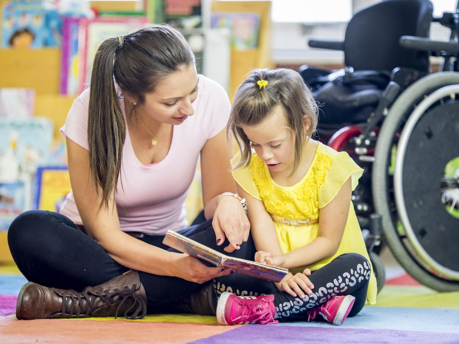 Eine Frau schaut sich gemeinsam mit meinem Mädchen im Rollstuhl ein Buch an.