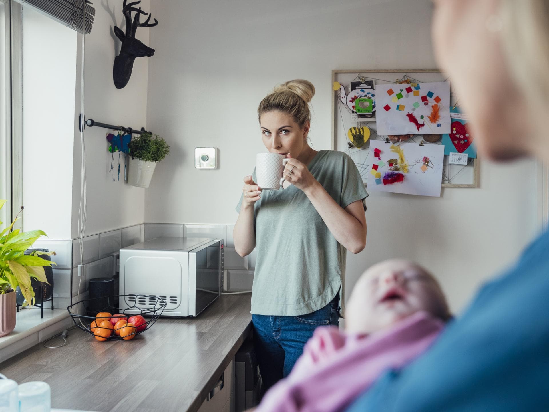 Mutter trinkt Tee, während die Oma das Baby hält.