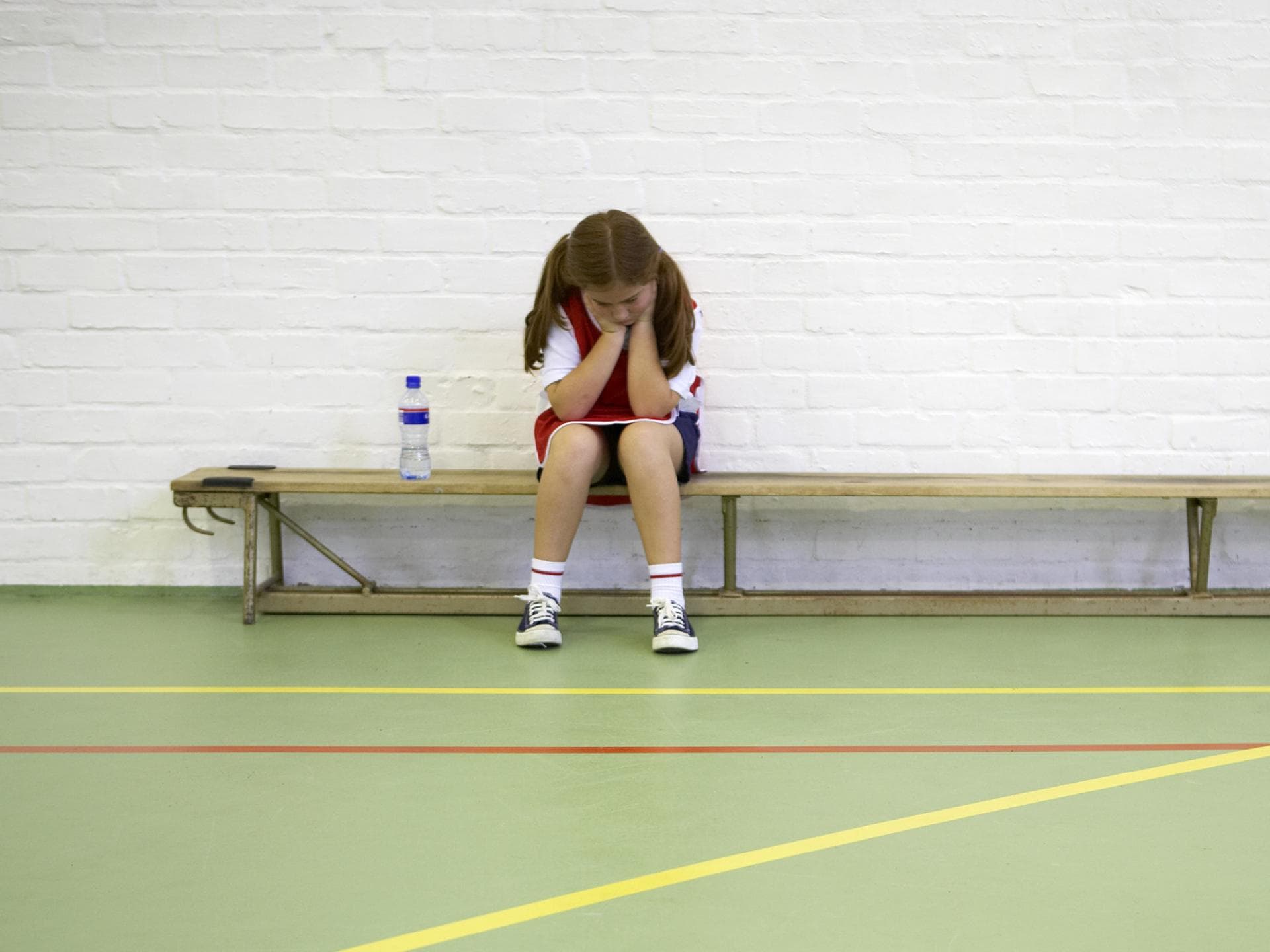 Ein Mädchen sitzt beim Schulsport frustriert auf der Bank. 