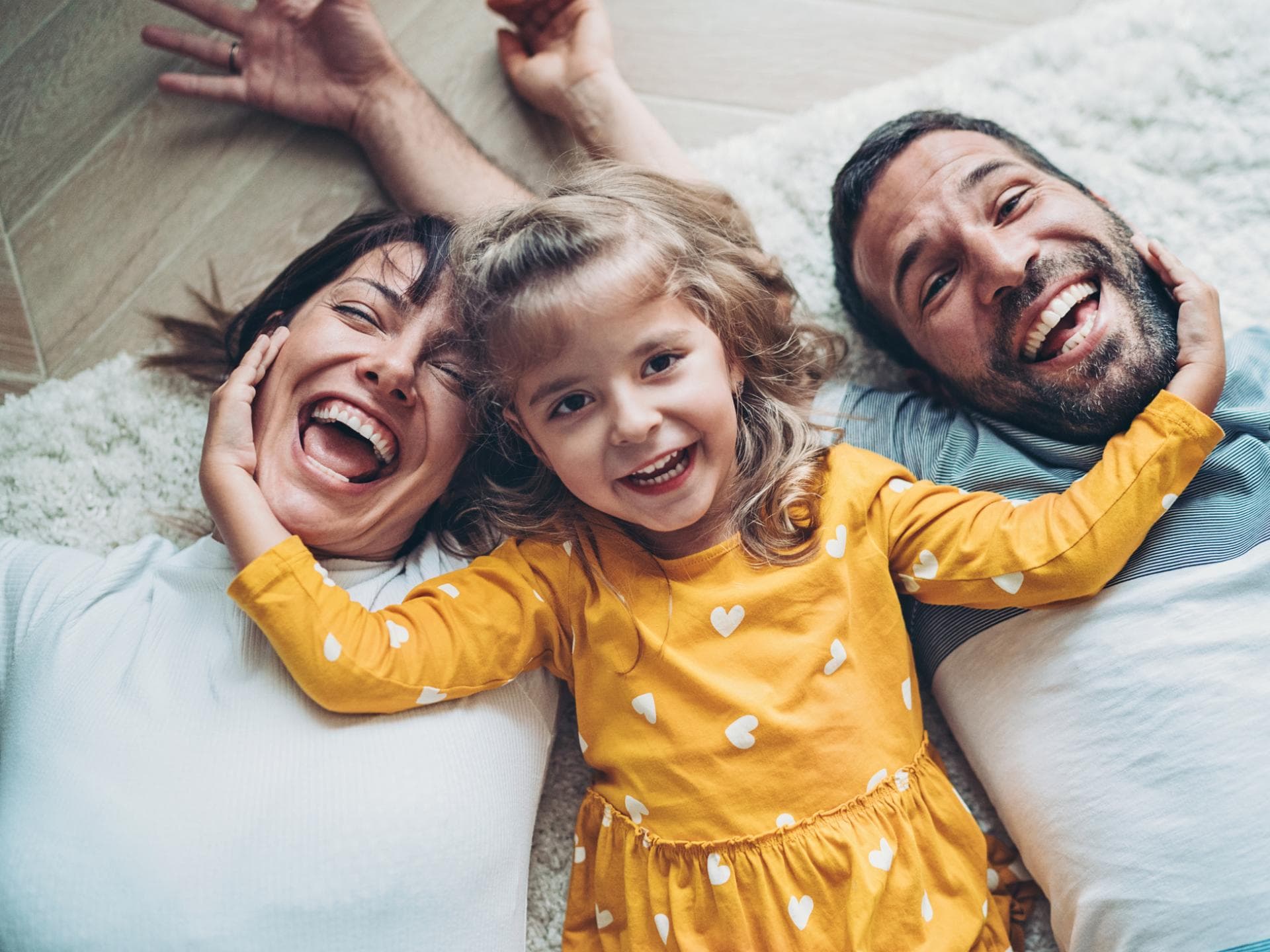 Lachende Eltern liegen mit ihrem Kind auf dem Boden.