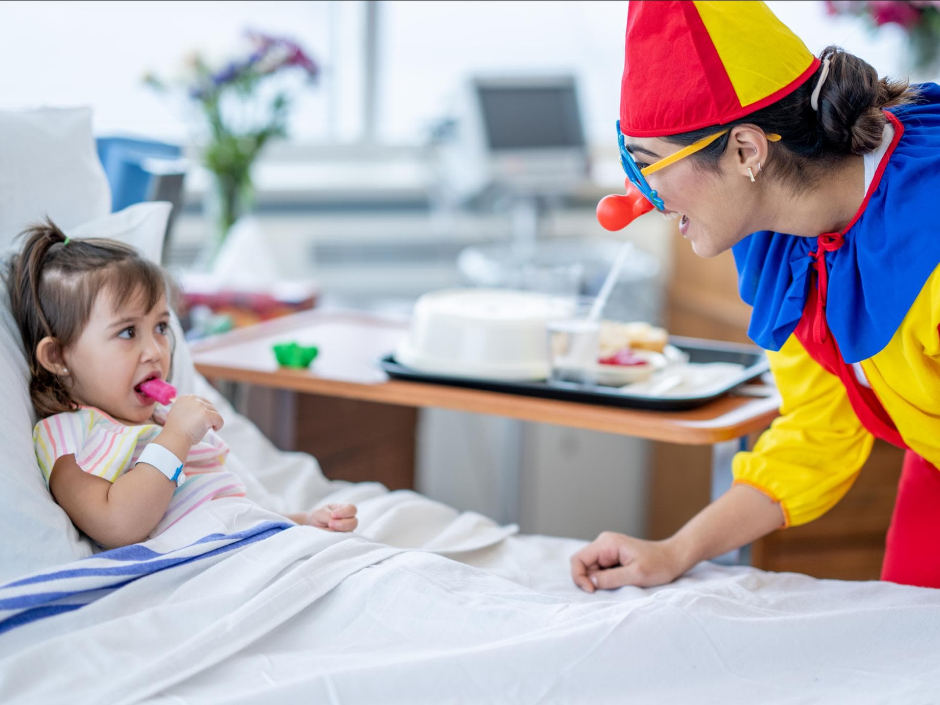 Ein weiblicher Klinik-Clown überrascht ein kleines Mädchen im Krankenhaus.