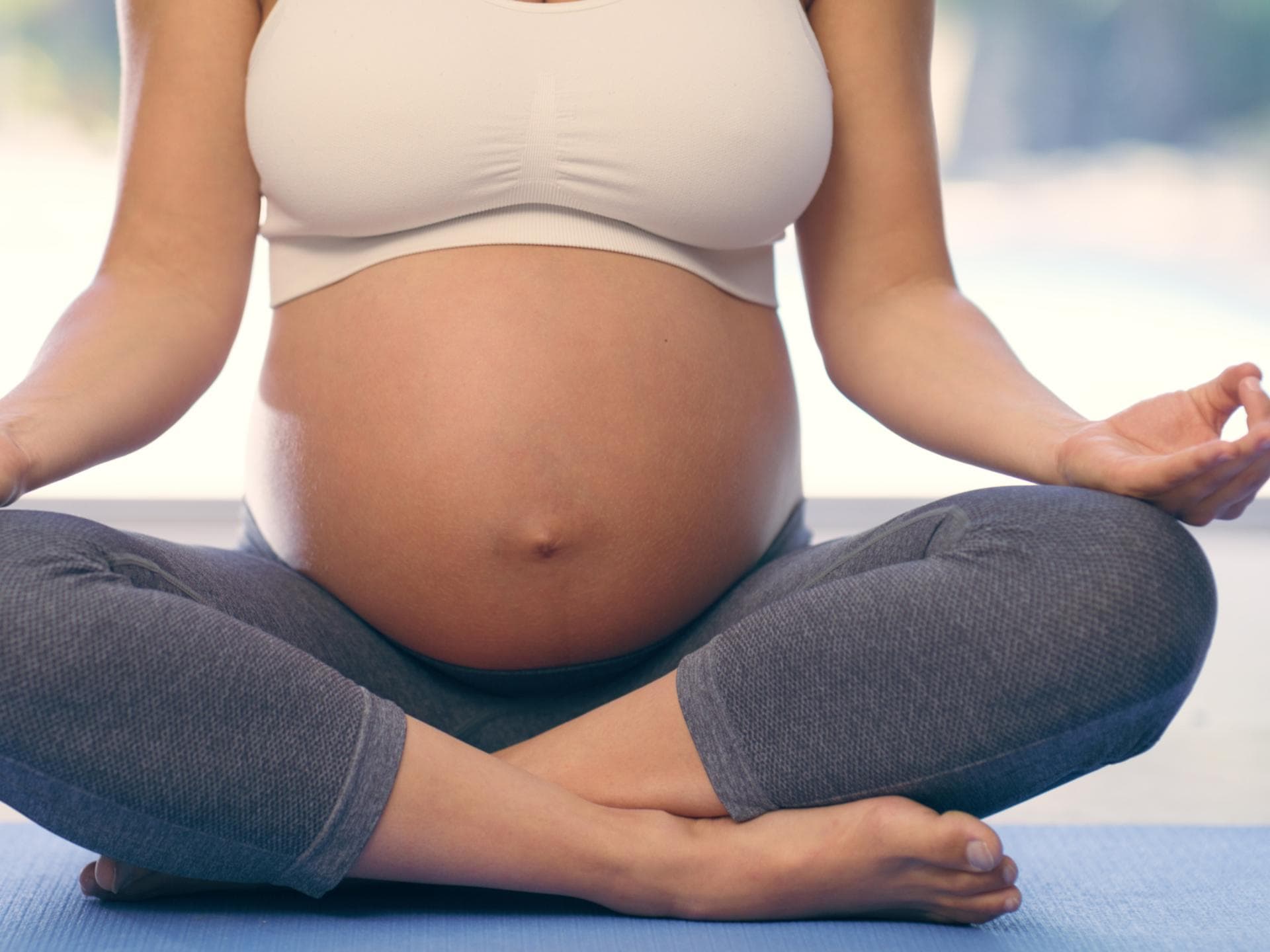 Hypnobirthing verspricht eine weitgehend schmerzfreie Geburt. Nahaufnahme von schwangerer Frau beim Yoga.