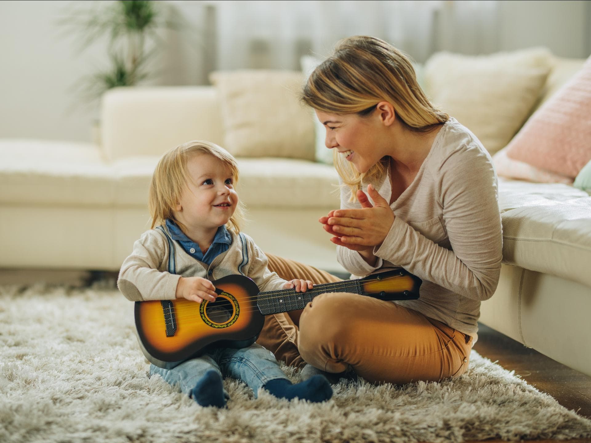 Eine Mama applaudiert ihrem kleinen Sohn, weil er Gitarre spielt