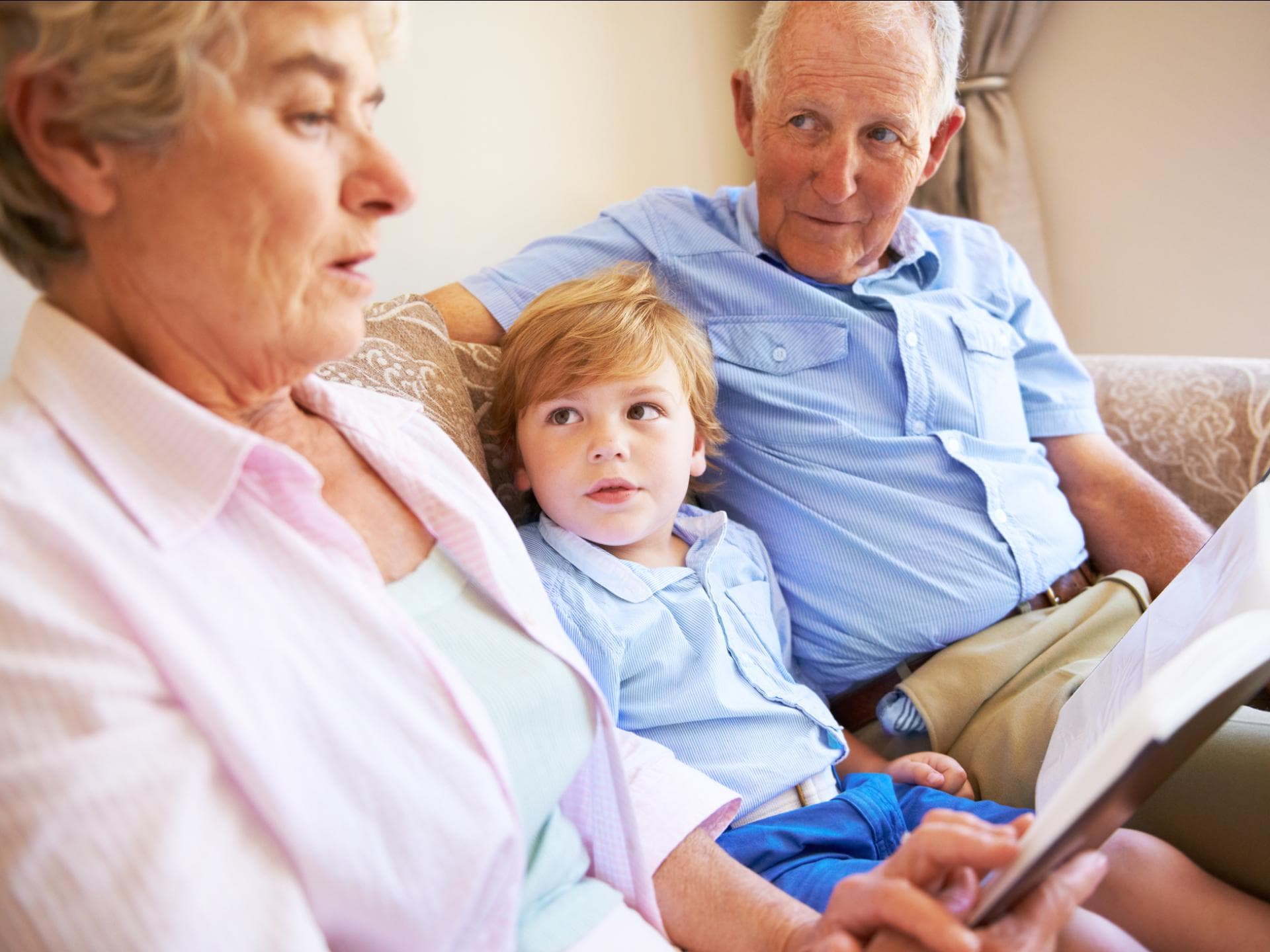 Oma und Opa lesen mit dem Enkel ein Buch. 