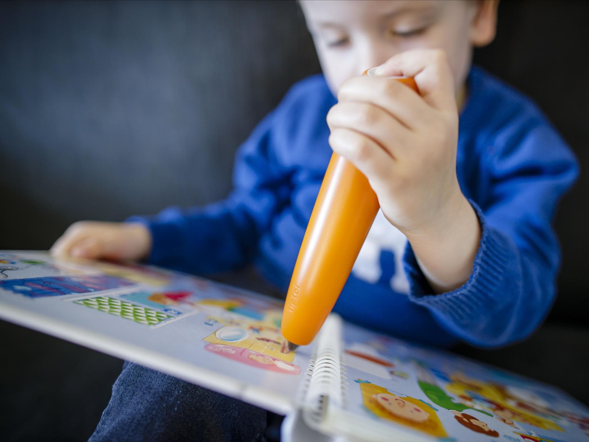 Ein kleiner Junge tippt mit einem orange farbenen Tiptoi-Stift auf ein Tiptoi-Buch.