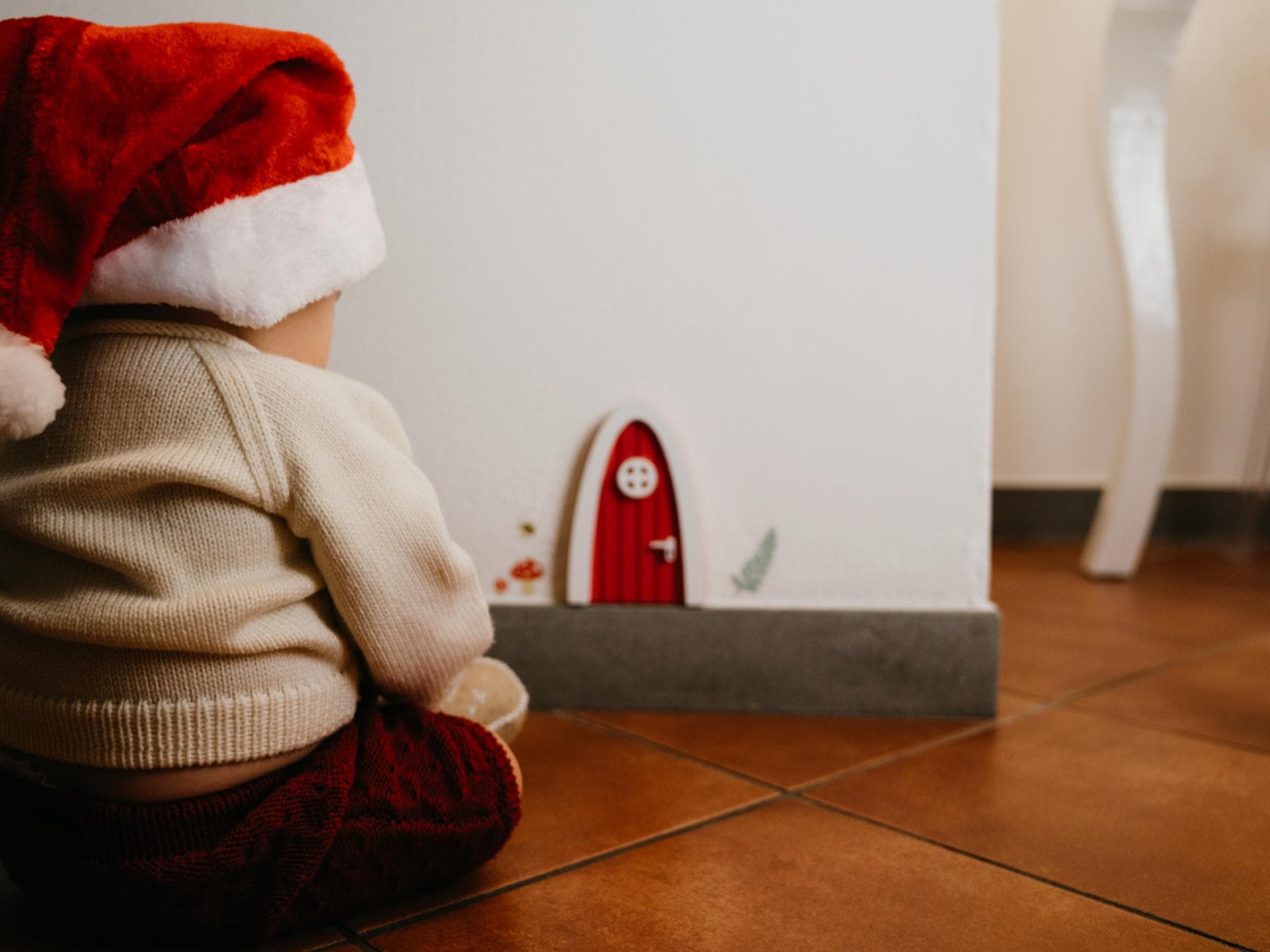Baby-Junge mit Weihnachtsmütze sitzt vor der weihnachtlichen Wichteltür
