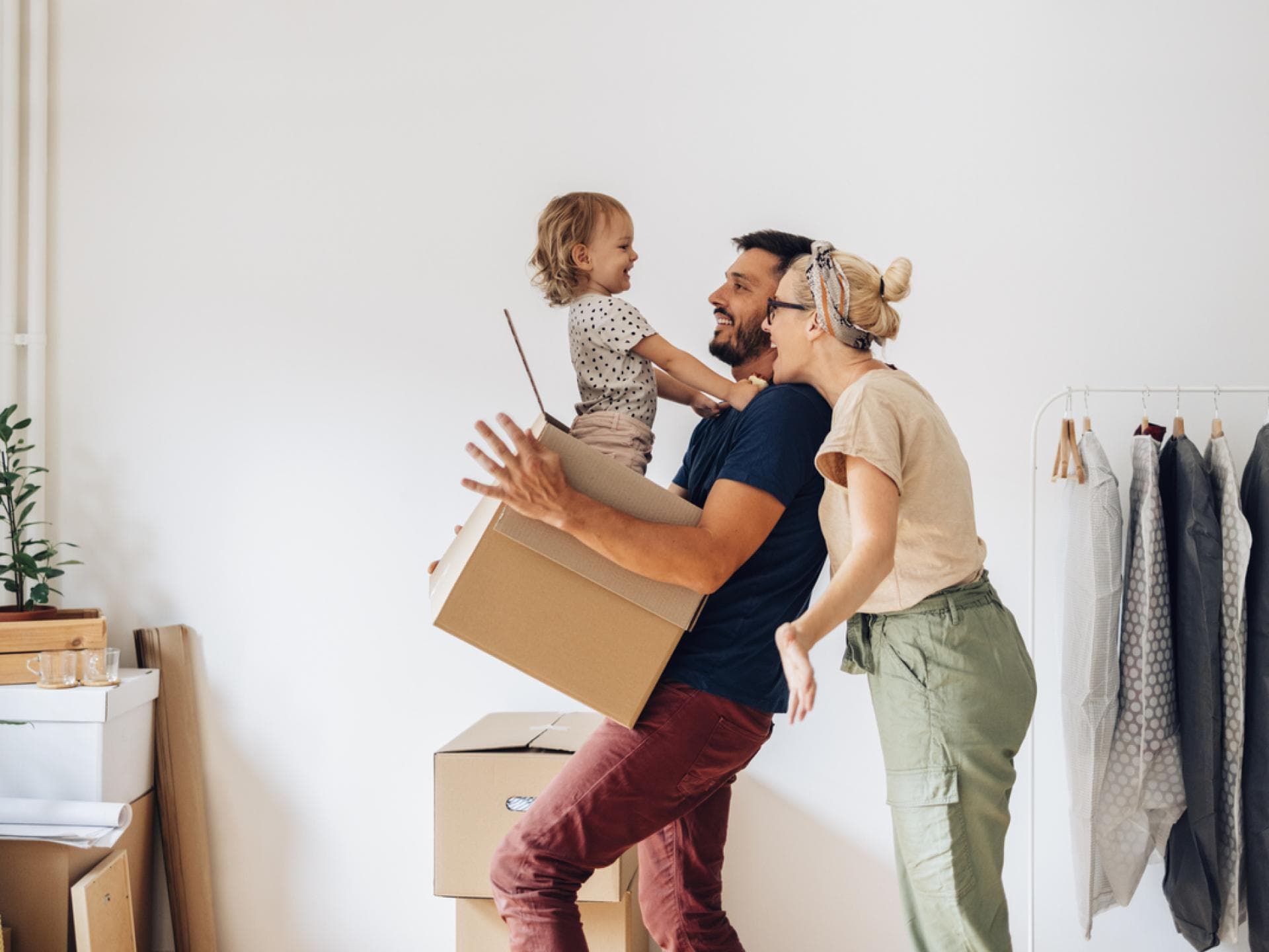 Fröhliche Familie zieht in ein neues Zuhause und das Kleinkind sitzt im Umzugskarton. 