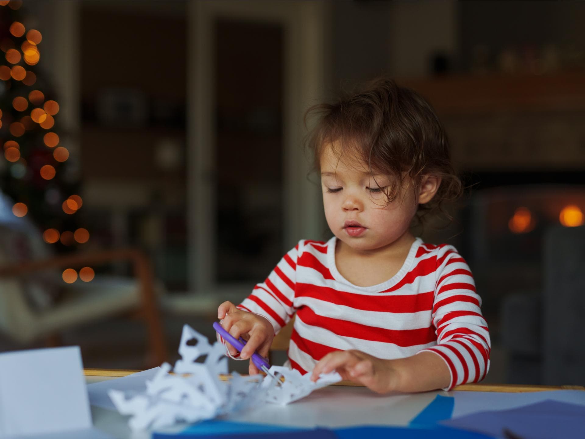 Einfache Weihnachtssterne basteln – so kann es klappen. Ein kleines Mädchen bastelt und schneidet Weihnachtssterne.