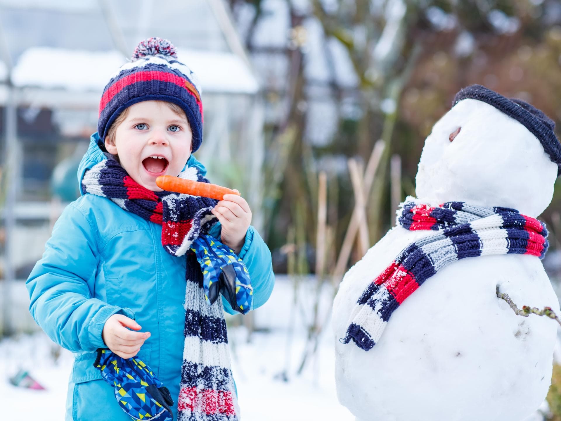 Damit Kinder gesund durch den Winter kommen, ist die richtige Ernährung ausschlaggebend. Kind beißt in die Möhre des Schneemanns.