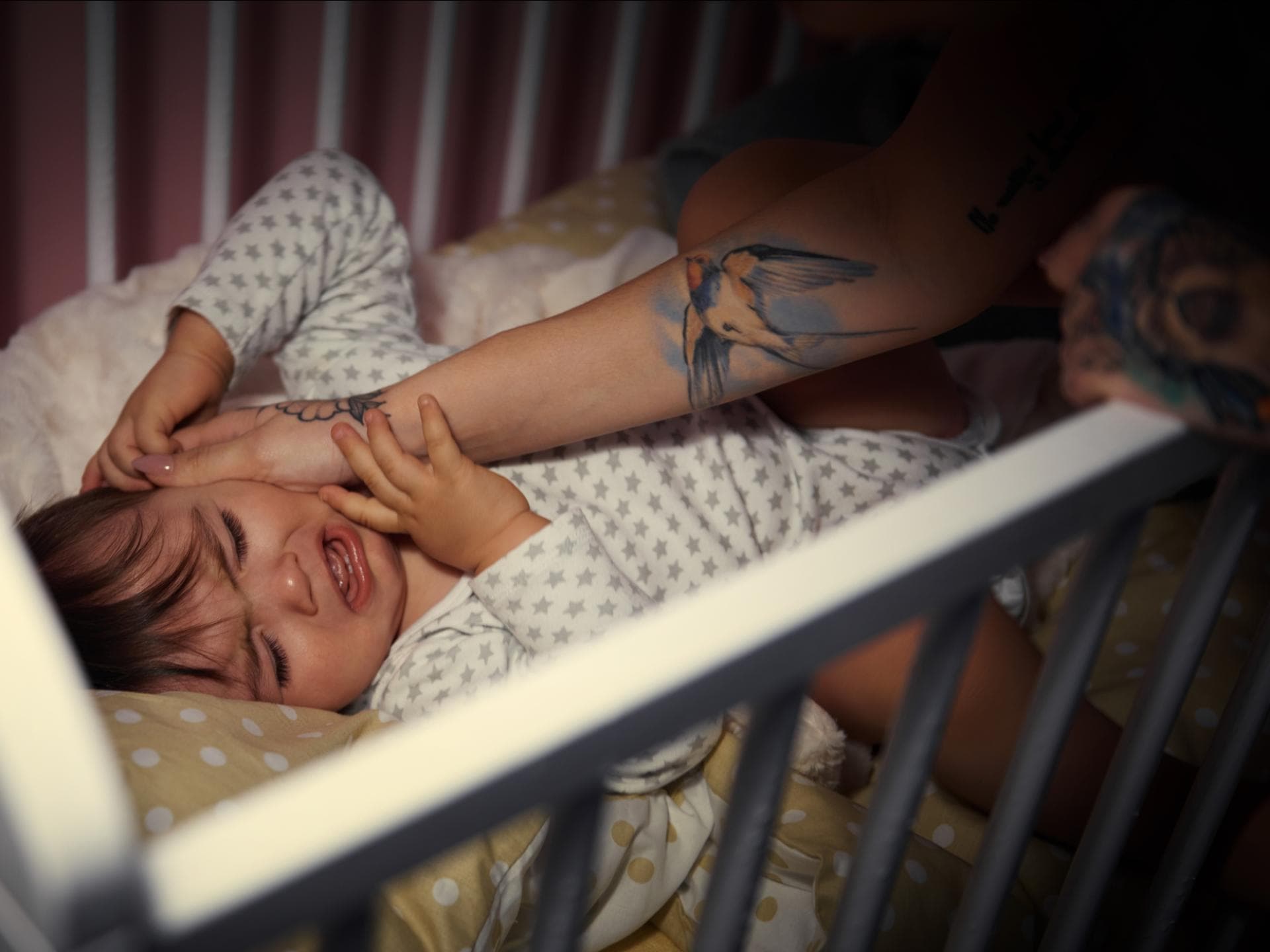 Ein weinendes Baby nachts im Babybett wird von Mutter gestreichelt. Ein weinendes Baby nachts im Babybett wird von Mutter gestreichelt.