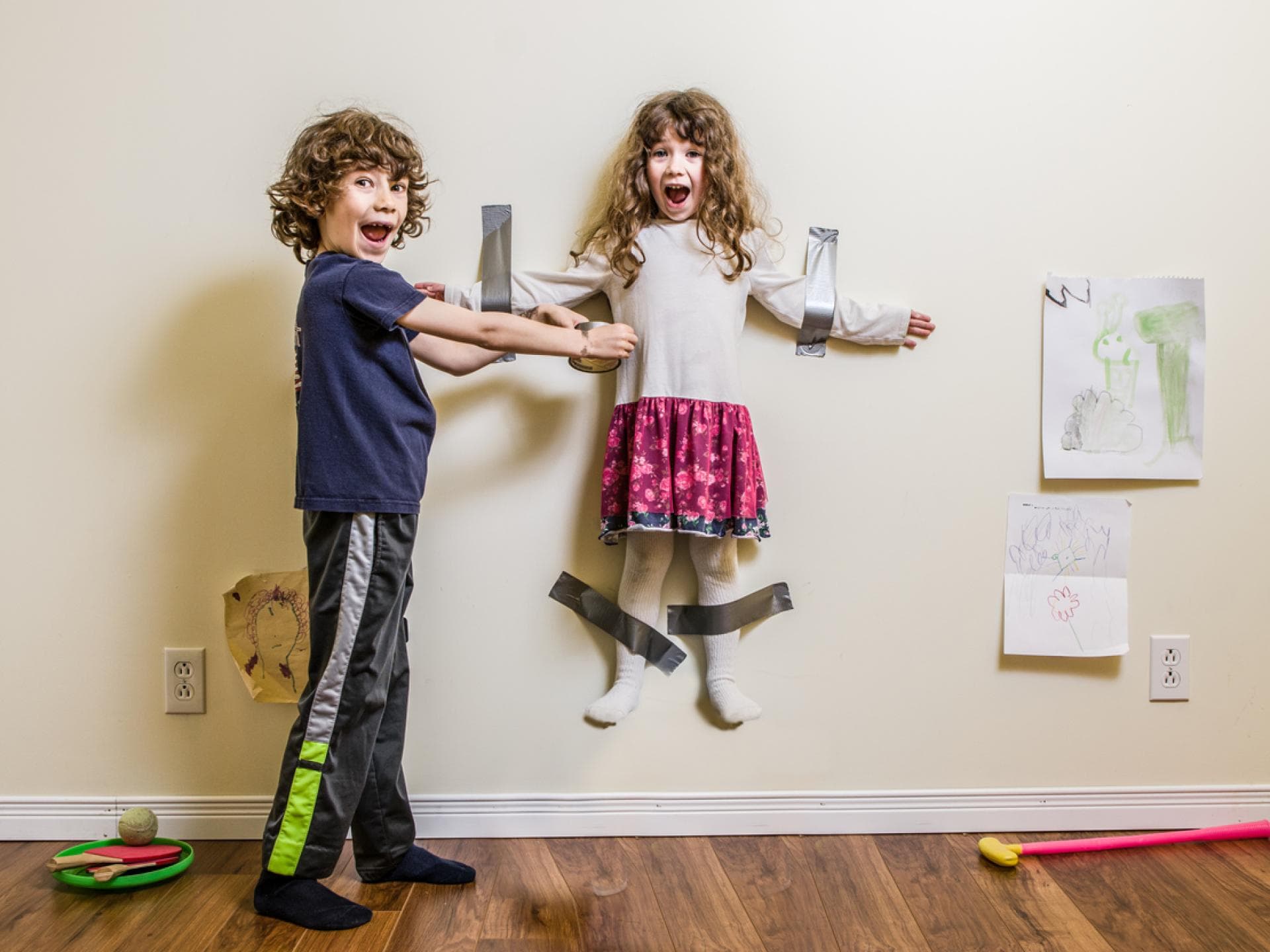 Junge klebt seine kleine Schwester im Spiel an der Wand fest.