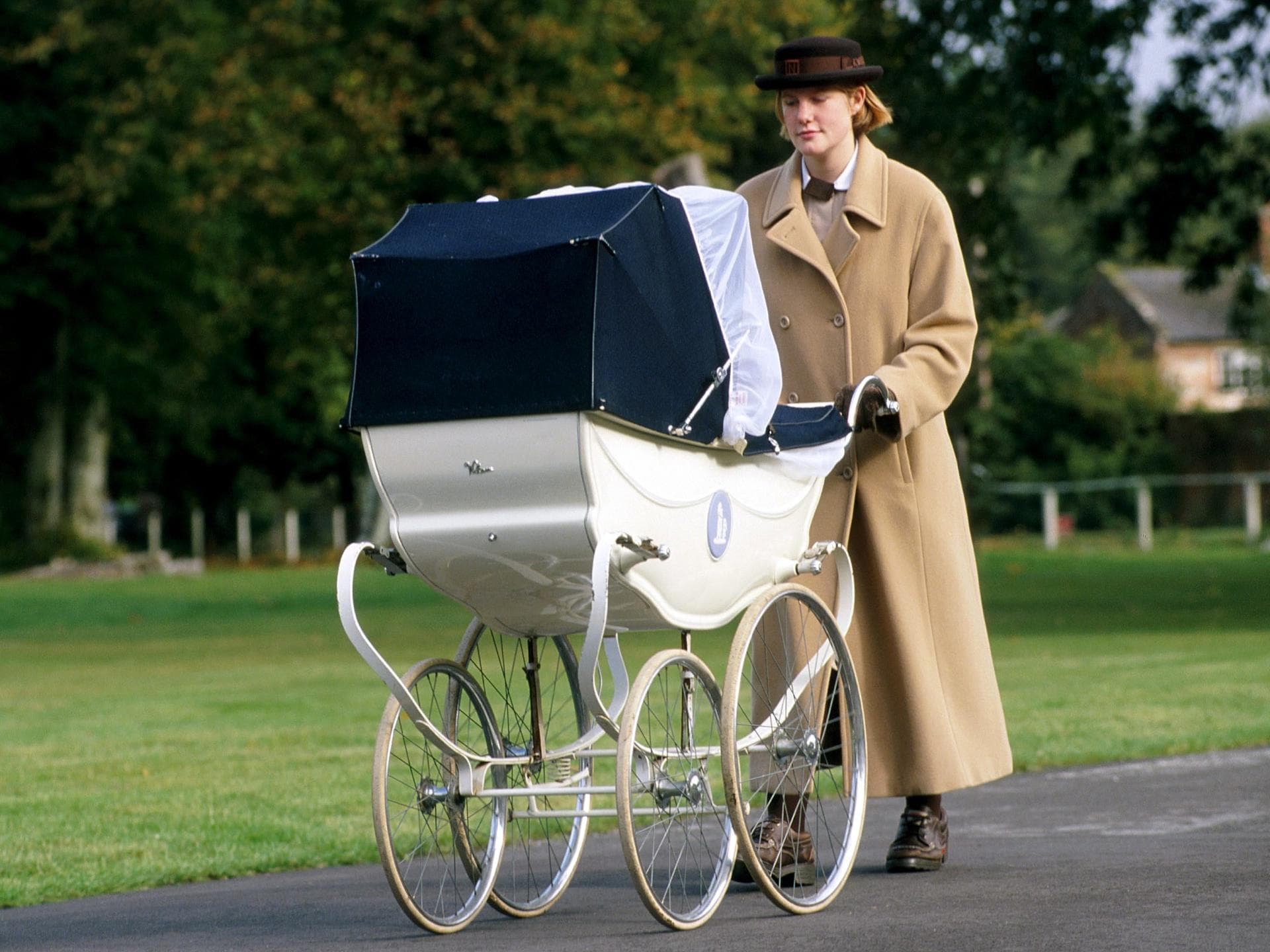 Eine Norland-Nanny schiebt ein Baby im Kinderwagen draußen durch die Gegend. Eine Norland-Nanny schiebt ein Baby im Kinderwagen draußen durch die Gegend.