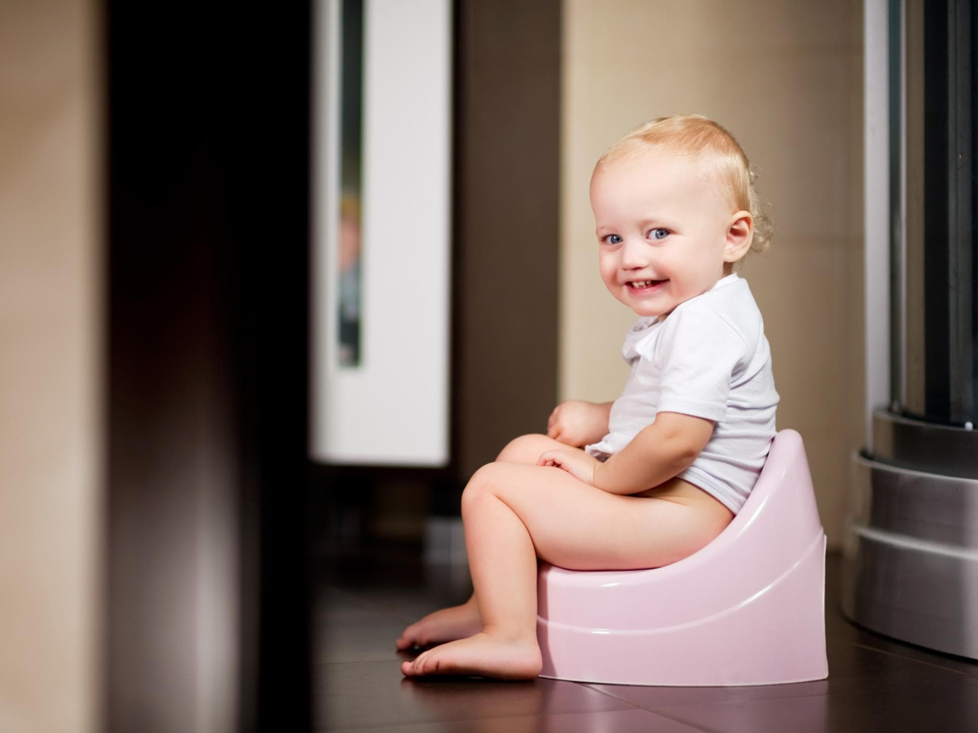 Kleines Mädchen sitzt auf einem Topf im Badezimmer und lächelt.
