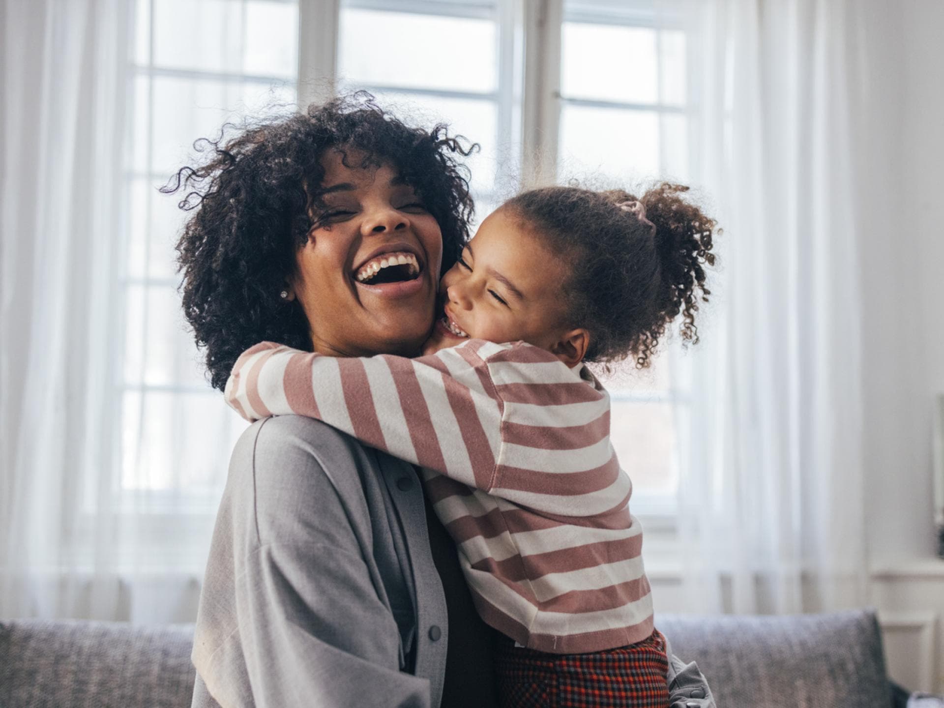 Eine Umarmung stärkt die Eltern-Kind-Bindung. Lachende Mutter wird von ihrer Tochter umarmt.