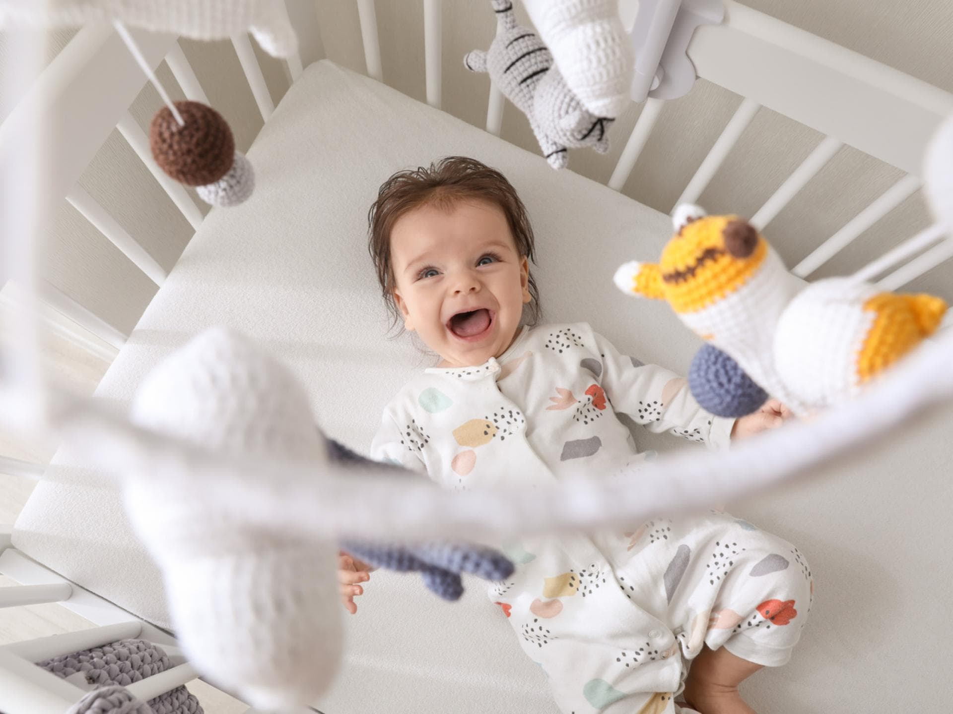 Baby liegt im Bett und lacht das über ihm hängende Mobile an. 