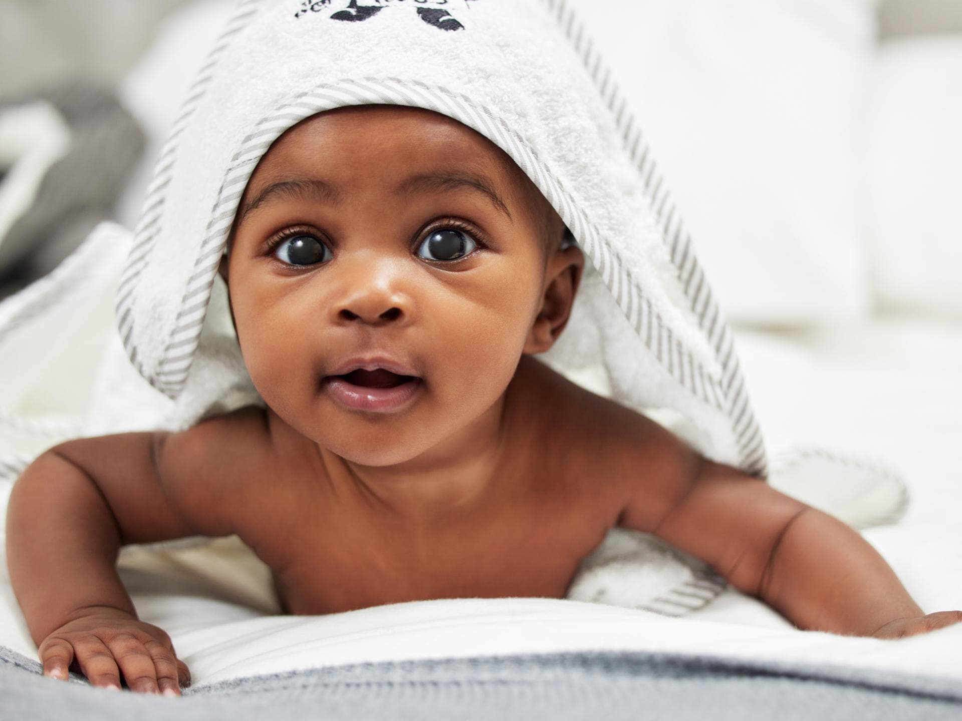 Niedliches, afrikanisches Baby unterm Kapuzenhandtuch.