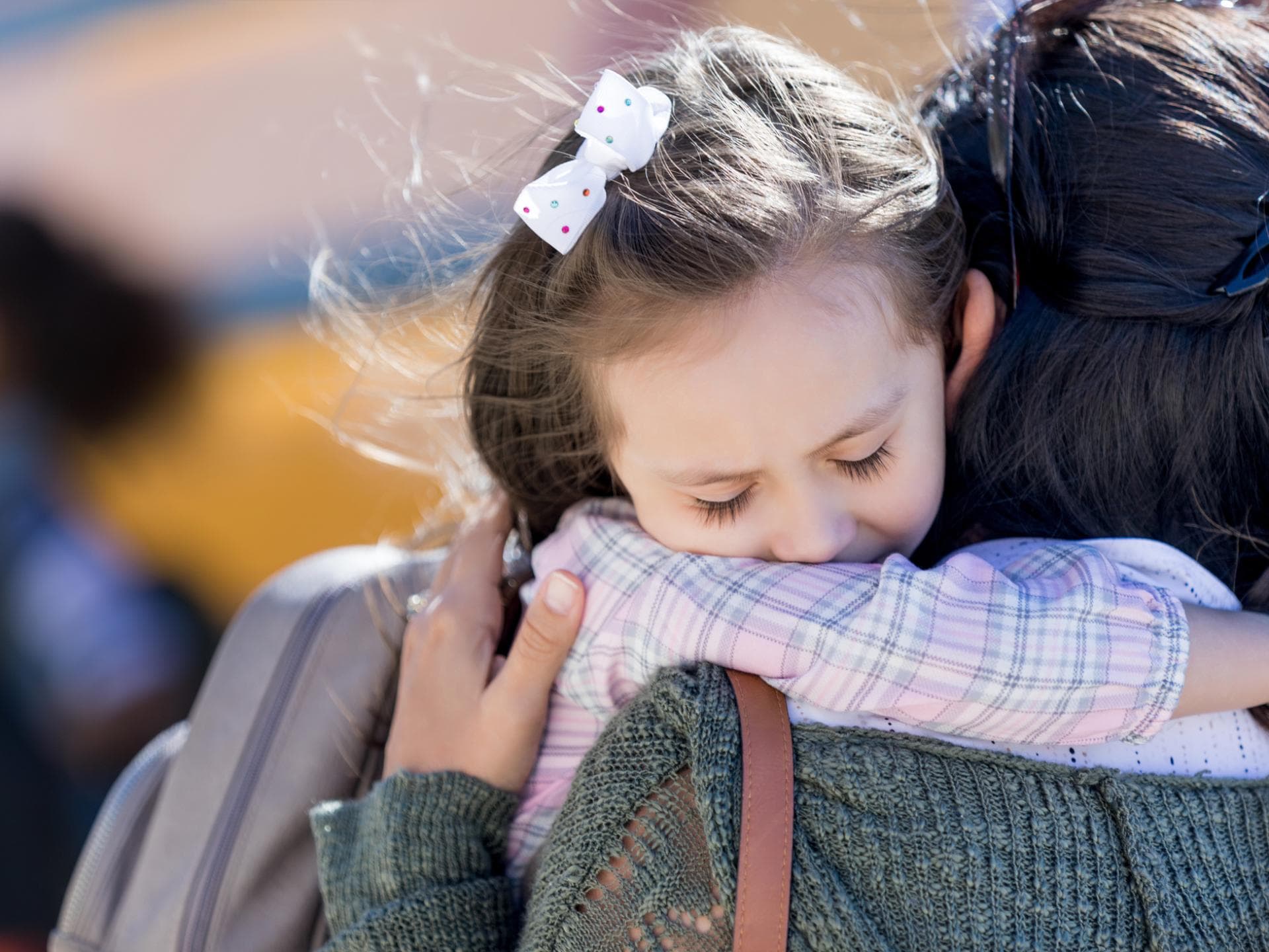 Angst vor der Klassenfahrt betrifft gerade jüngere Kinder. Ein junges Mädchen klammert sich vor dem Schulbus an seine Mama.