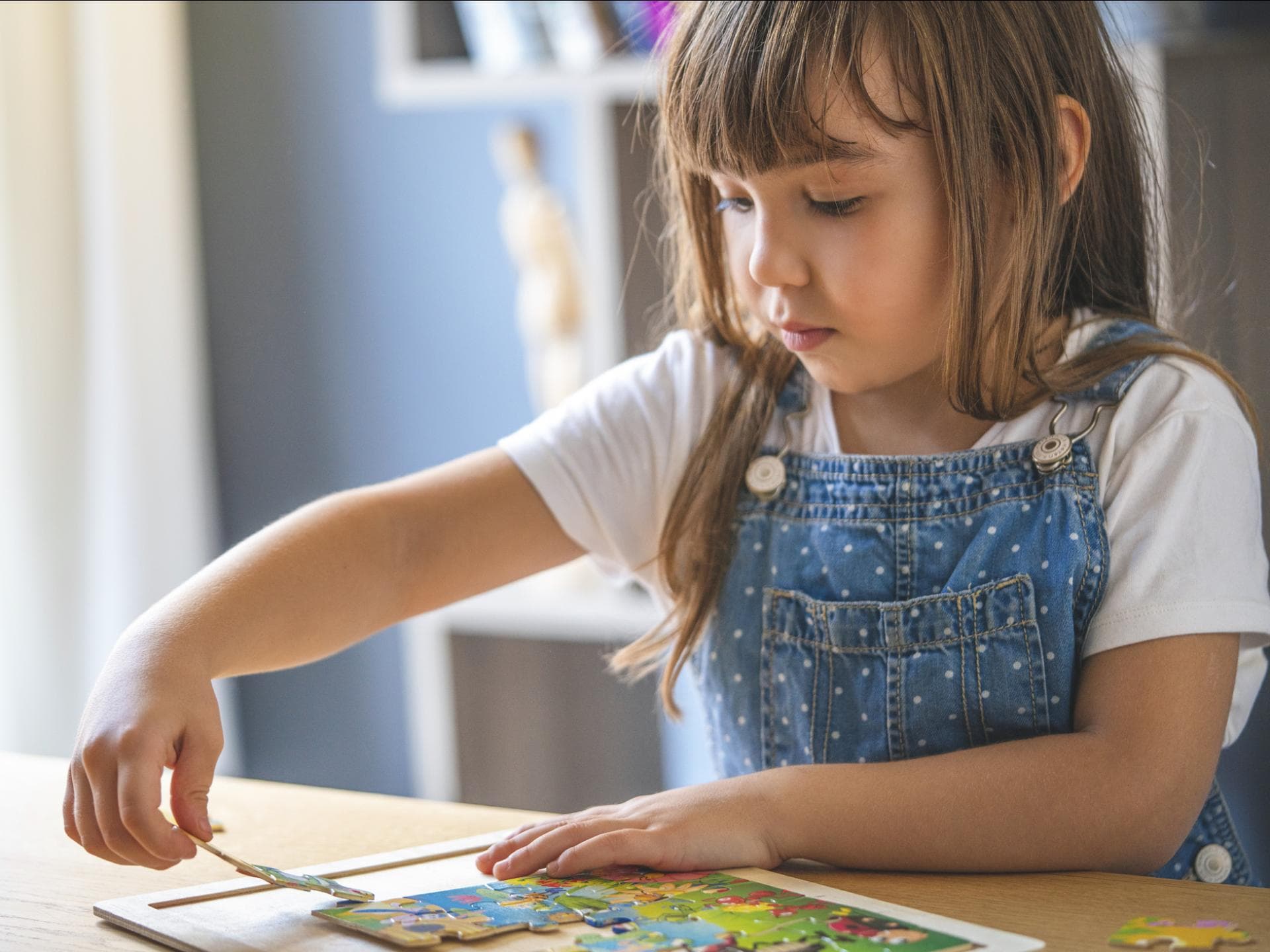 Puzzle sind bei Kleinkinder total beliebt. Ein kleines Mädchen sitzt am Tisch und puzzelt.