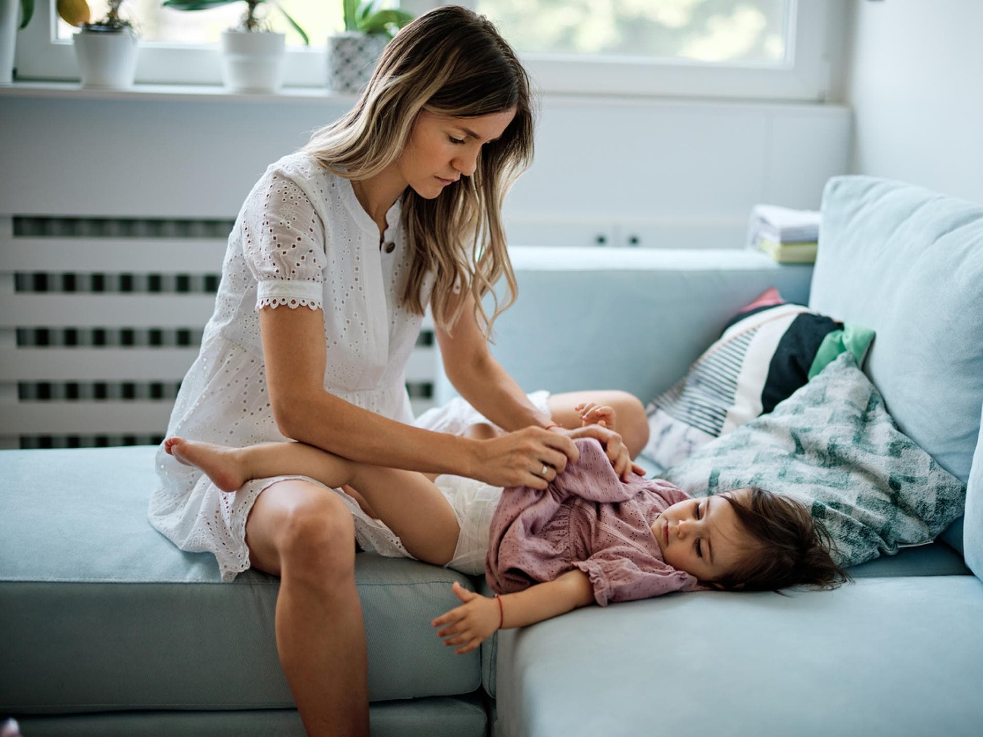 Junge Mutter wickelt ihre kleine Tochter auf dem Sofa. 