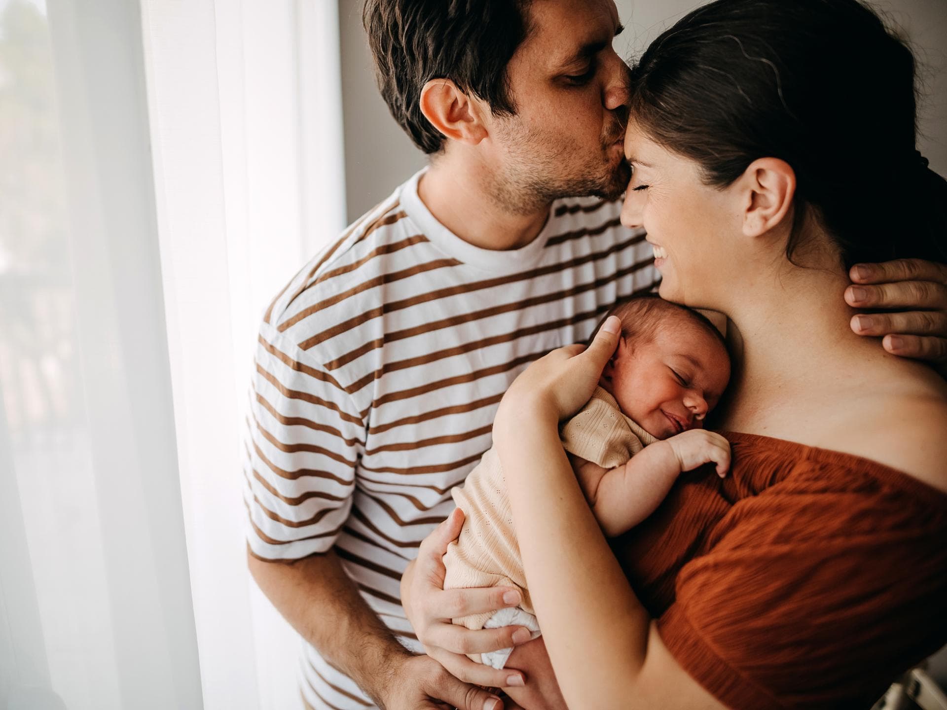 Paar mit Baby im Arm küsst sich.