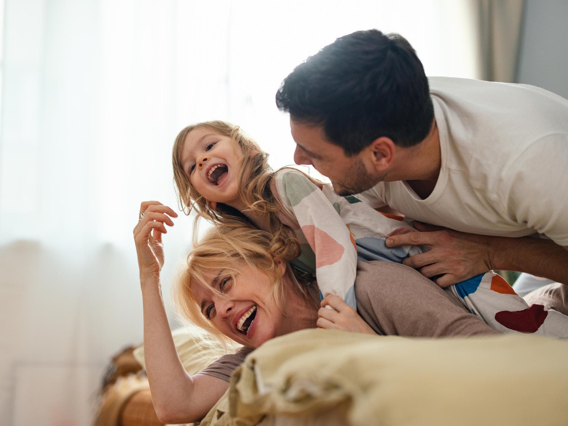 Eltern und Kind liegen im Familienbett und lachen.