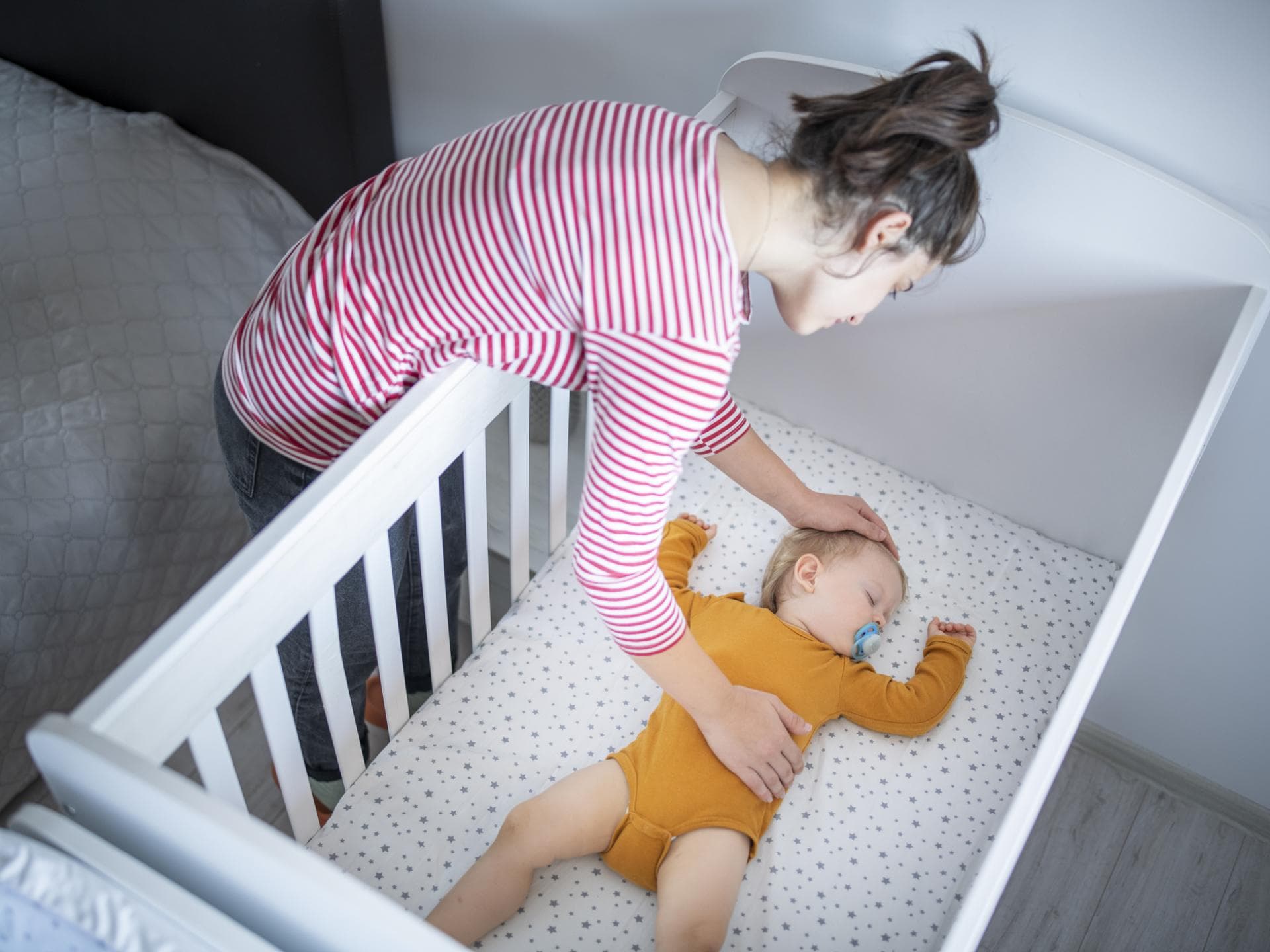 Mutter legt ihr schlafendes Baby ins Bett.