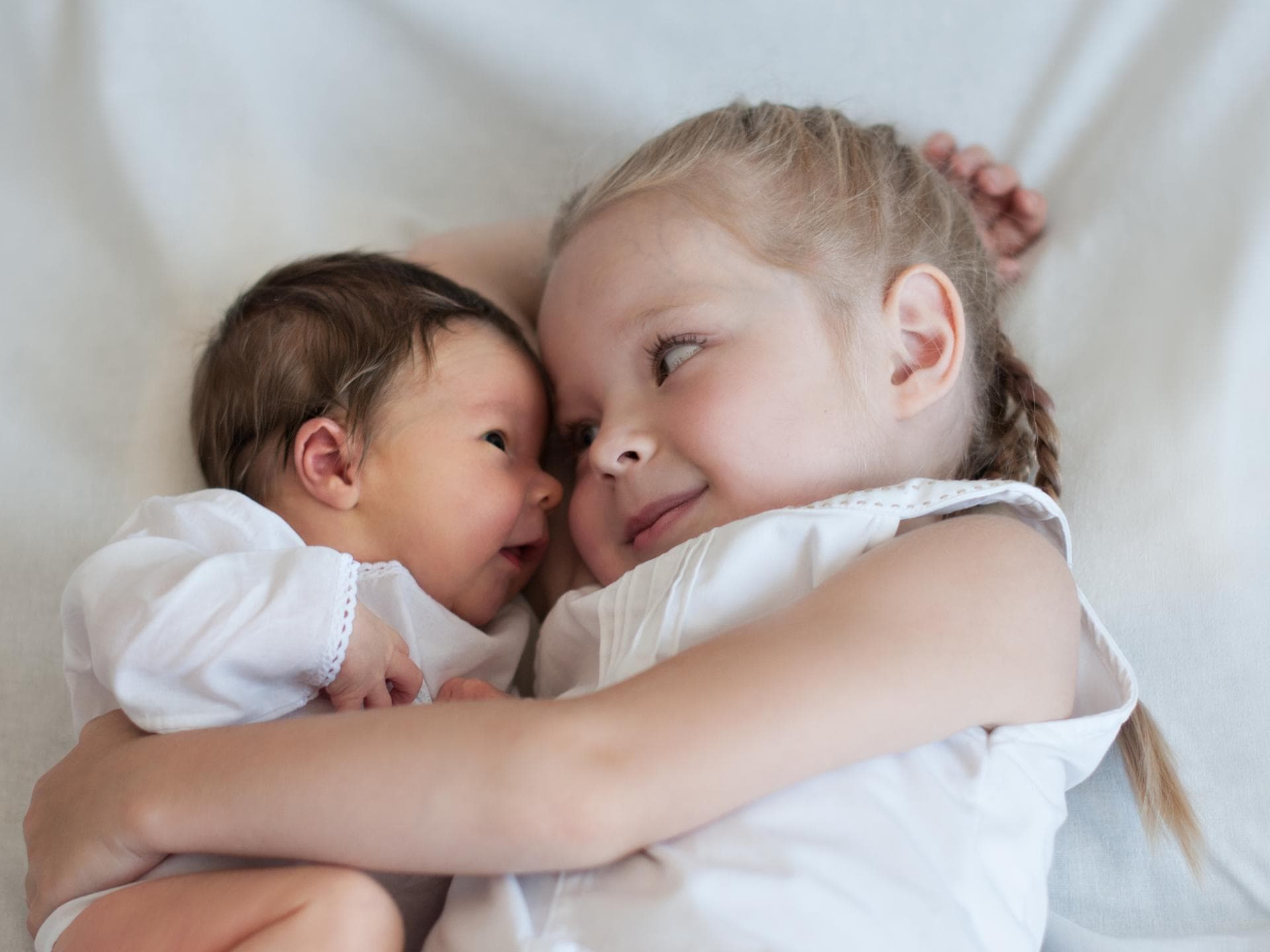 Älteste Töchter kommen laut einer Studie früher in die Pubertät. Mädchen hält Baby im Arm.