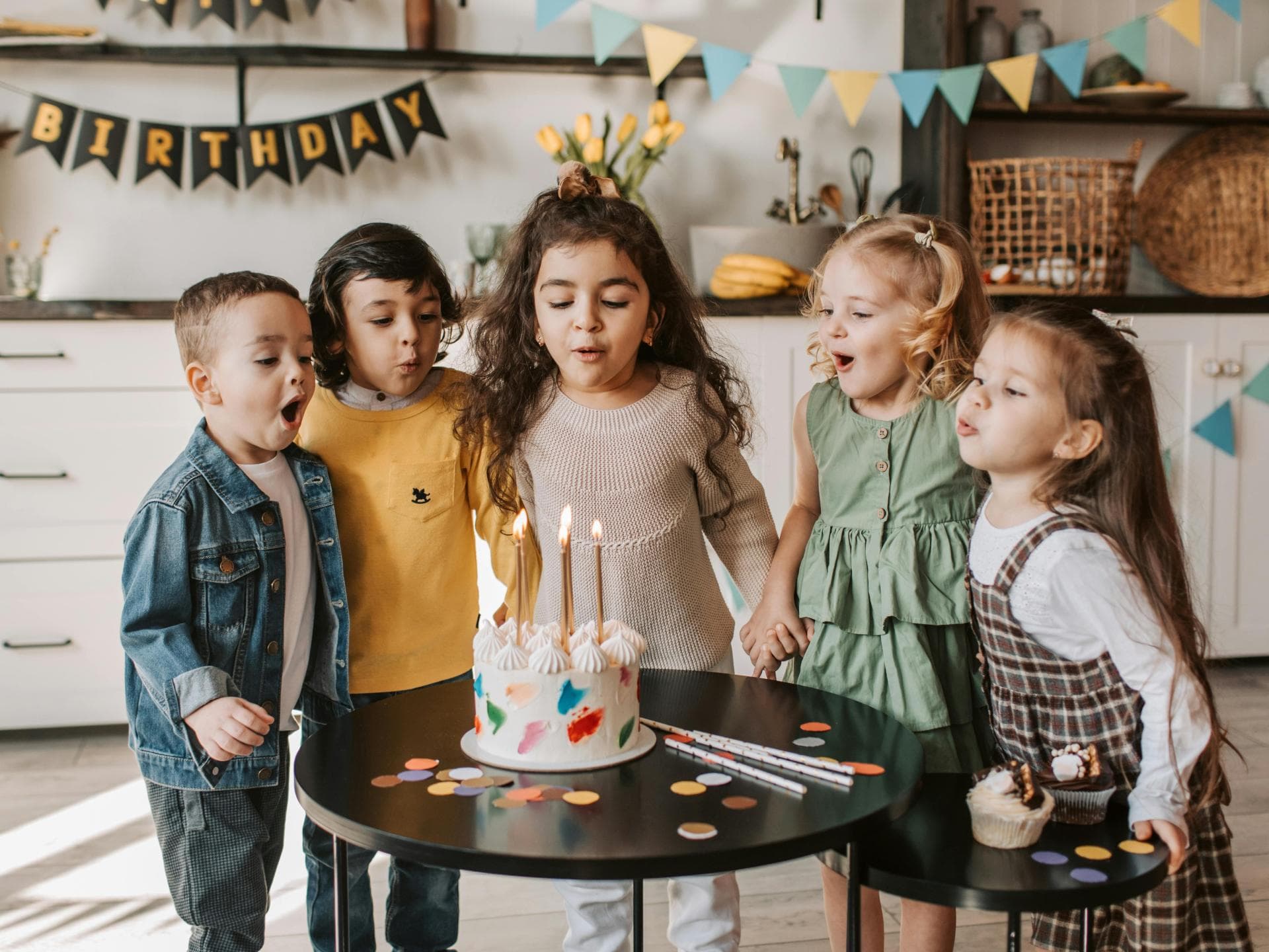 Drei kleine Mädchen und zwei kleine Jungs feiern Kindergeburtstag ohne Eltern.