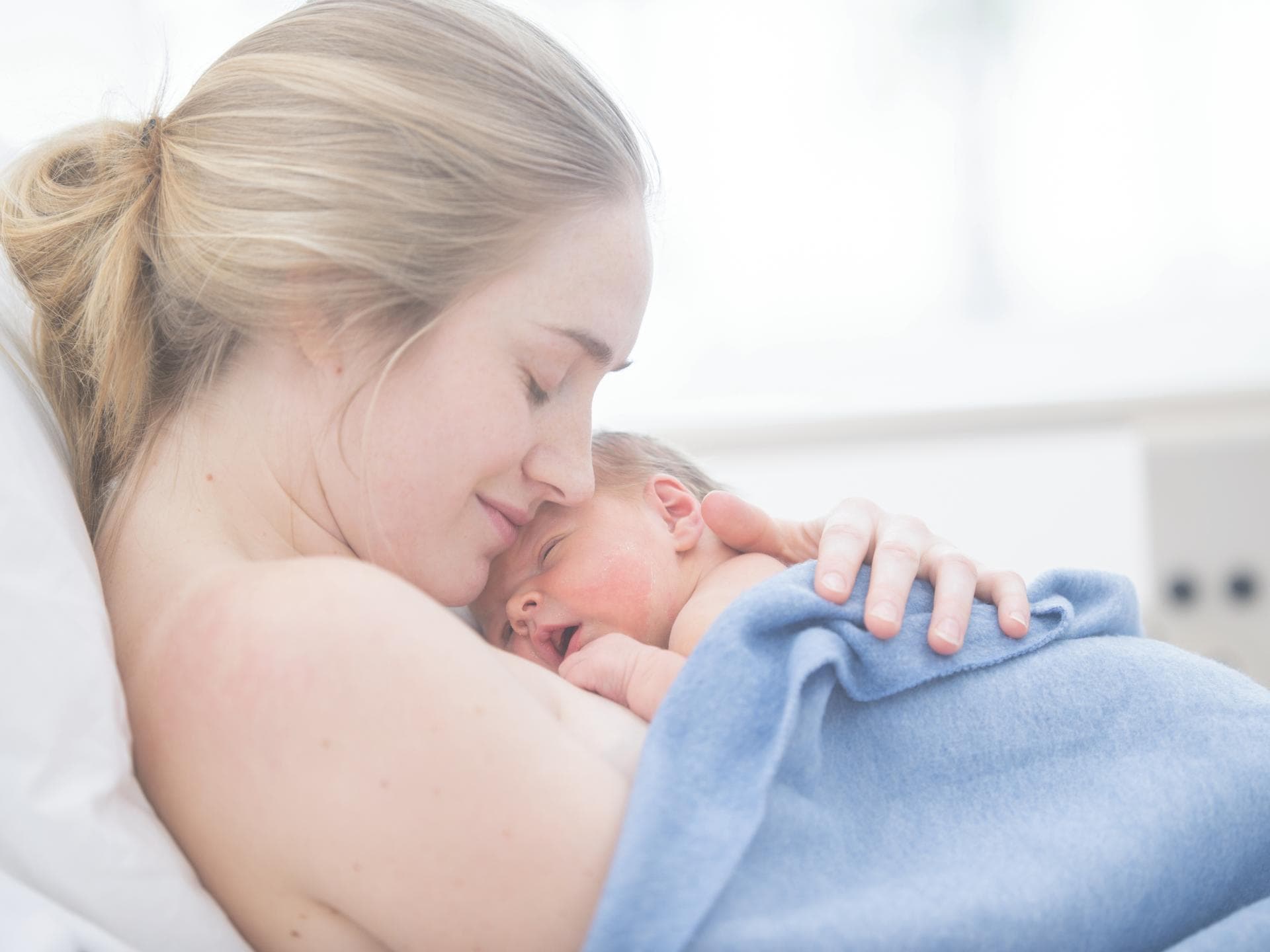 Frau liegt mit Baby auch der Brust im Wochenbett.