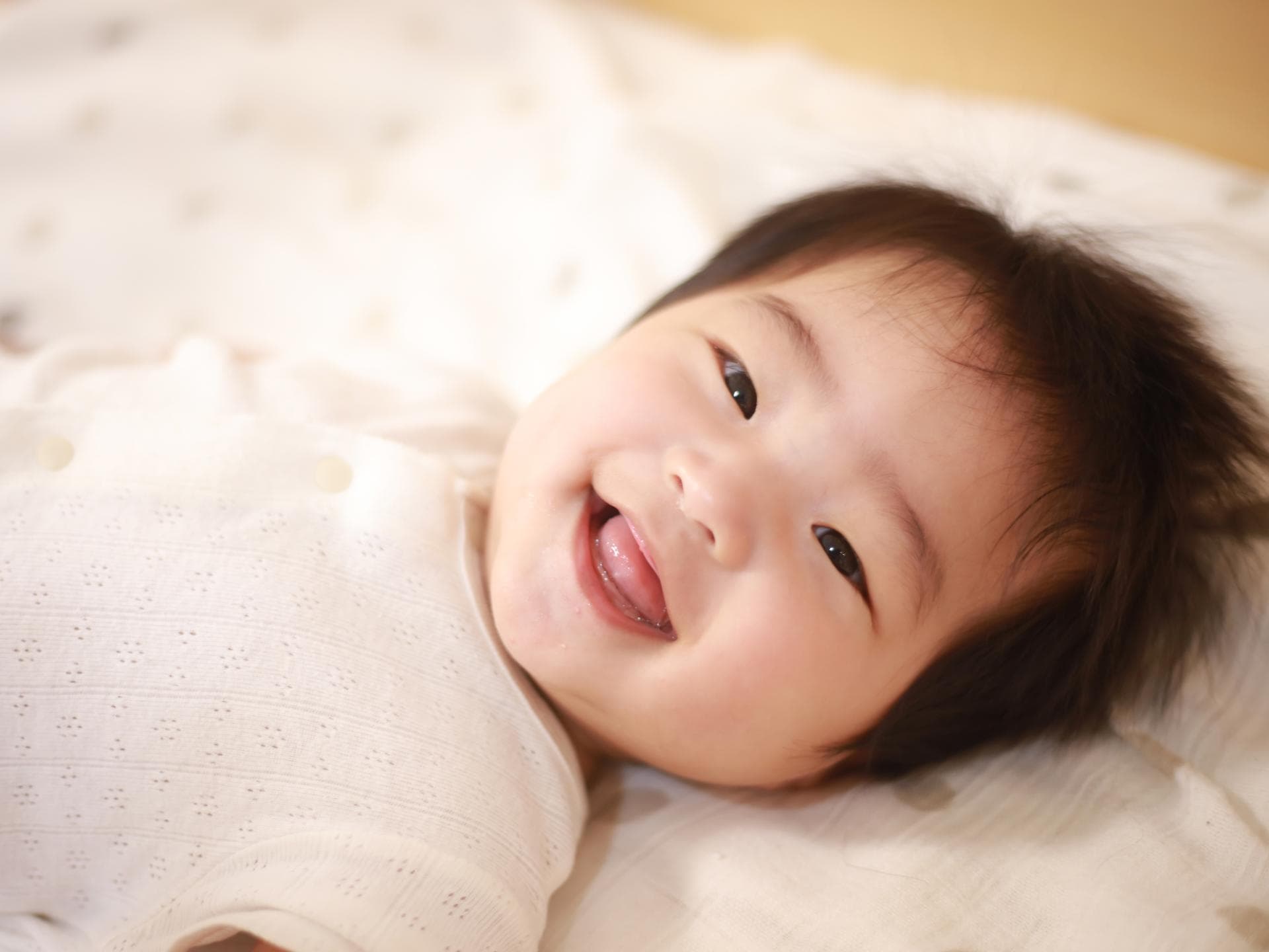Japanische Jungennamen haben einen wunderschönen Klang. Japanisches Baby liegt lachend im Bett.